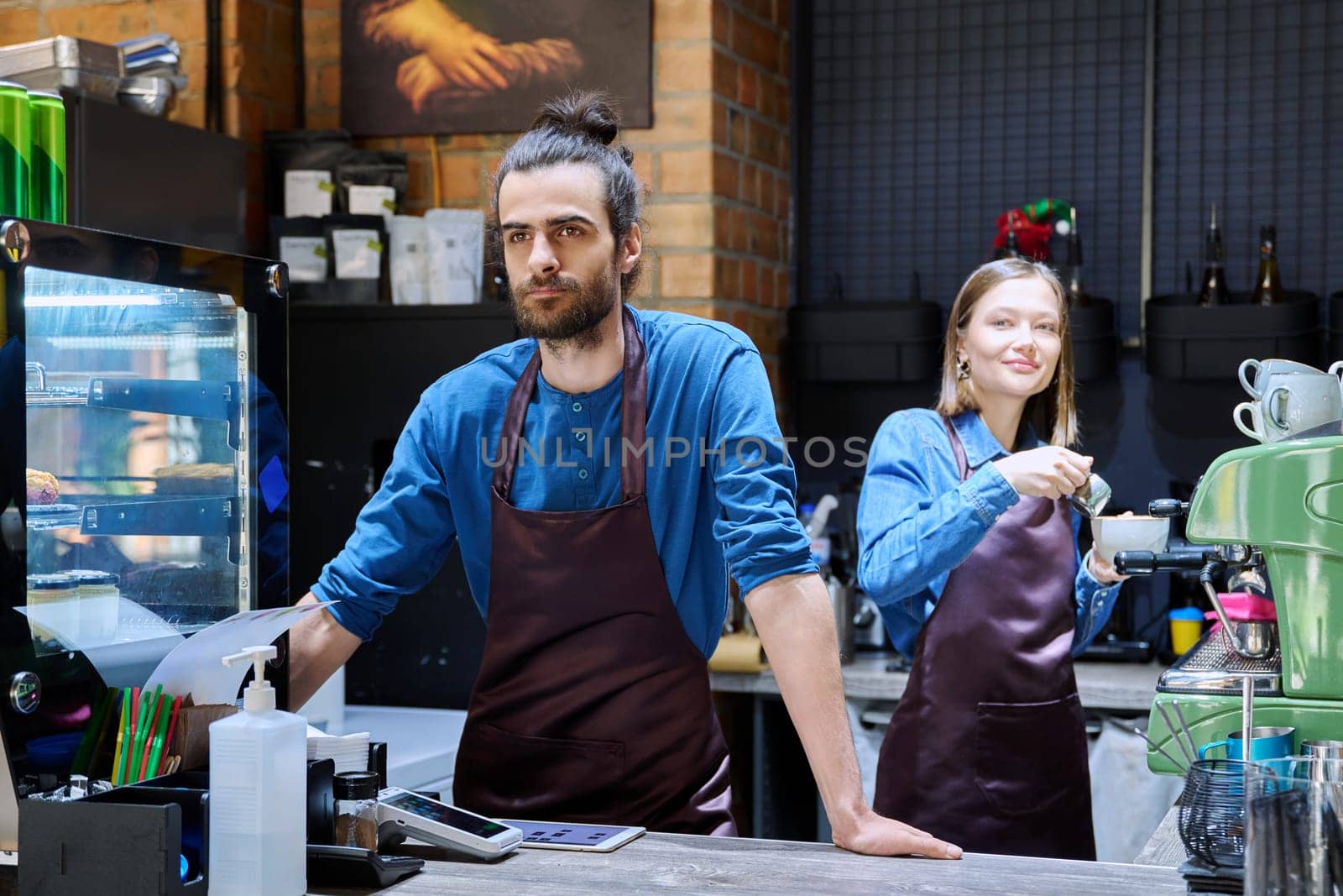 Business team colleagues partners young man woman in aprons working together in workplace behind counter in restaurant coffee shop cafeteria. Cooperation staff partnership teamwork work small business