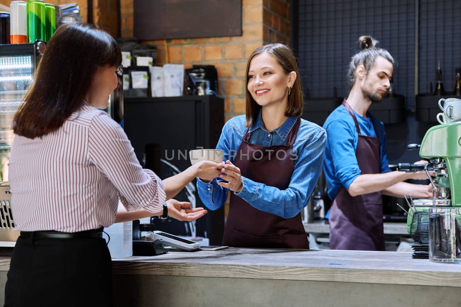 Woman customer of coffee shop near counter with cup of coffee talking to restaurant workers owners. Workplace at bar, colleagues, partners in food service, work, entrepreneurship, small business