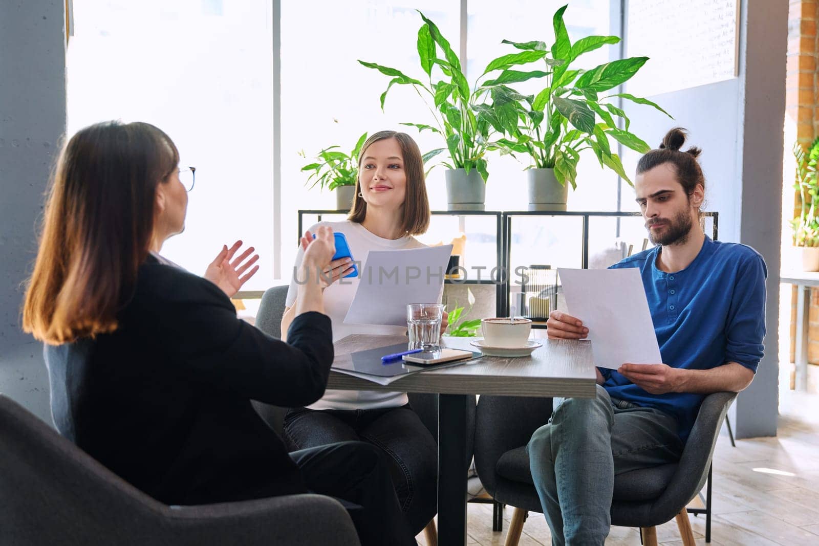 Couple of young clients at meeting with agent insurer realtor, reading paper contract by VH-studio