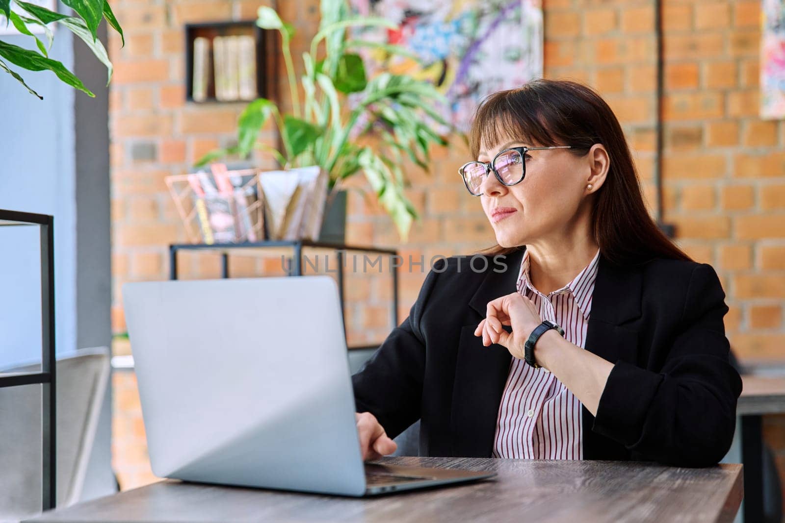 Middle-aged business confident successful serious woman working remotely at table with laptop computer in coworking cafe. Business, mature people, success, leadership, management, empowerment concept