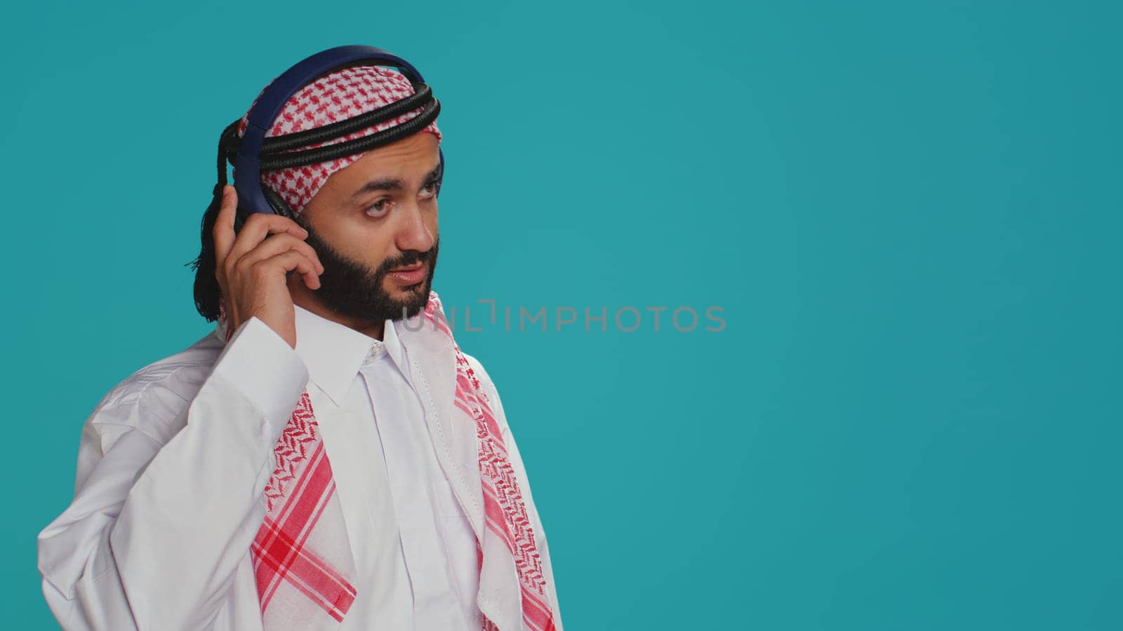 Groovy adult dancing around on camera, listening to funky songs on audio headset and having fun in studio. Middle eastern person in traditional islamic attire showing fun dance moves.