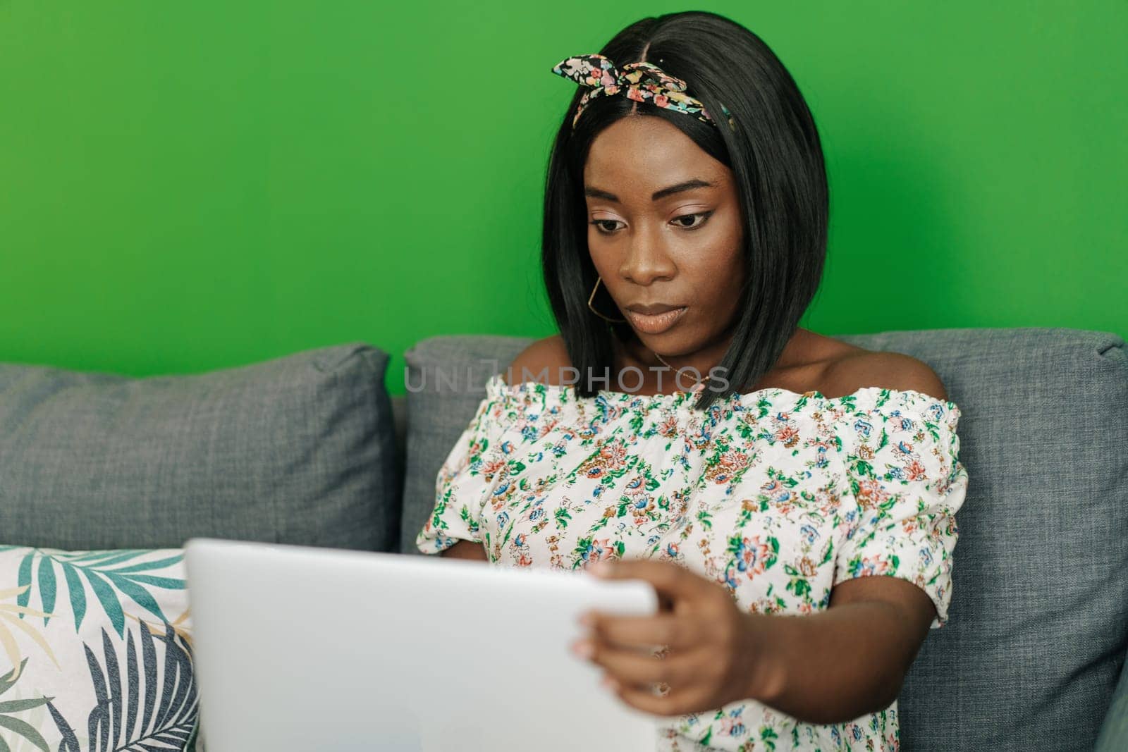 Young african woman working on laptop computer at home sitting on sofa close up