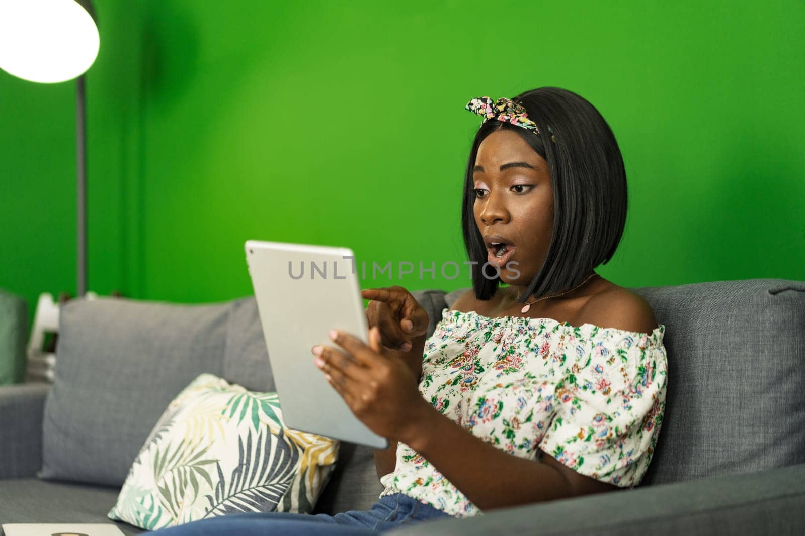Young African woman using digital tablet while resting at home on sofa