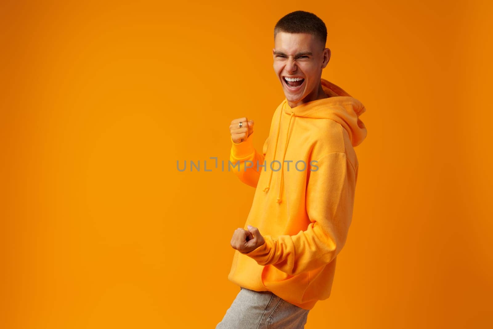 Portrait of a happy young man celebrating success against yellow background in studio