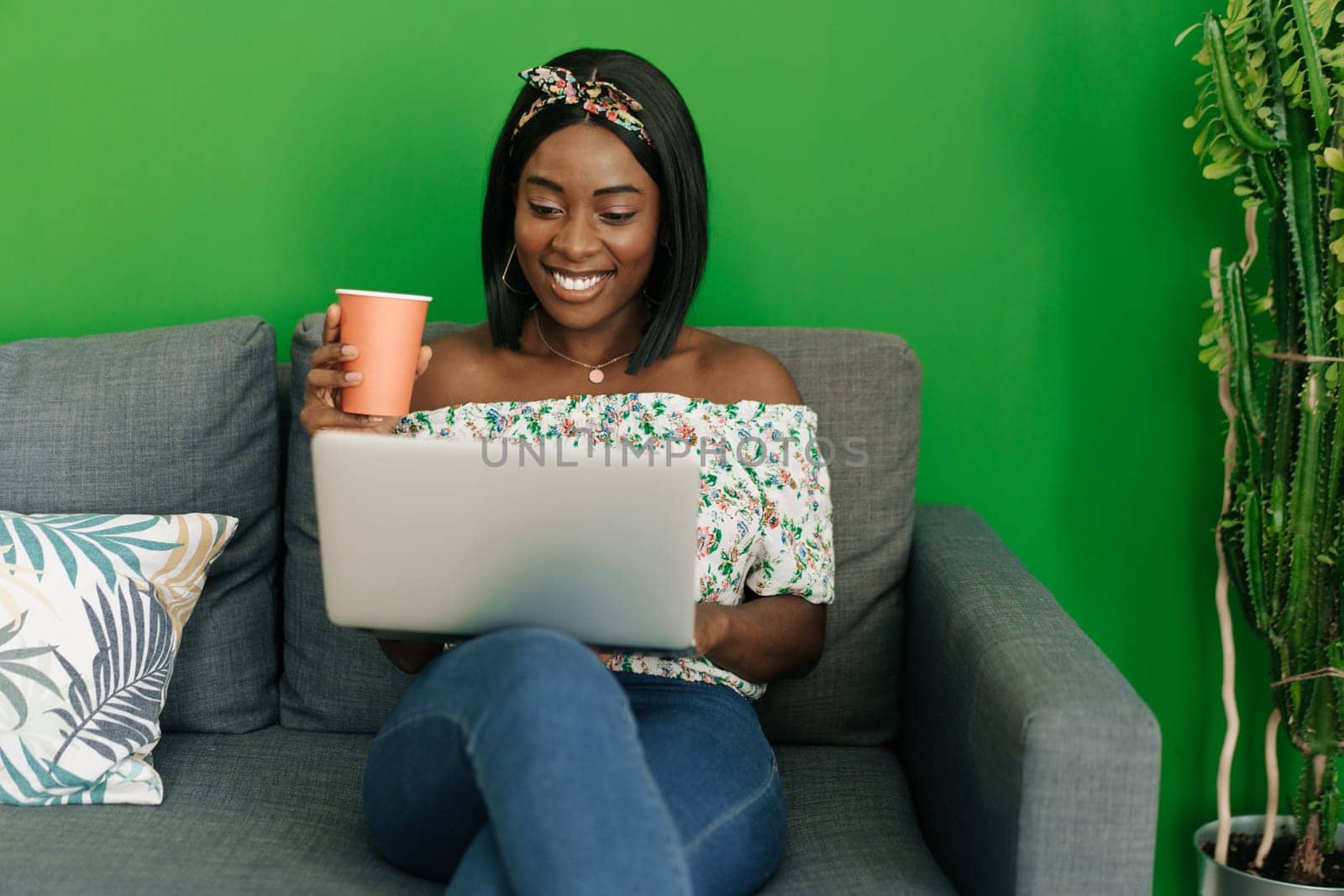 Young african woman working on laptop computer at home sitting on sofa close up