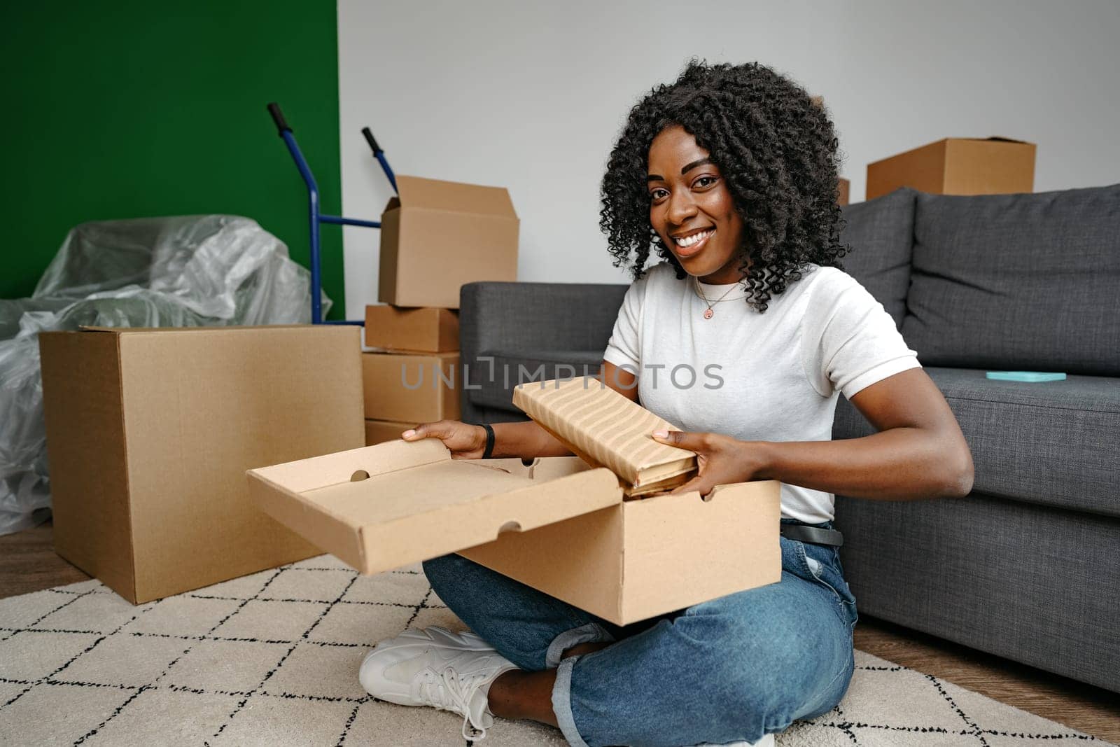 Young african woman sit on couch at home unpacking parcel cardboard box with online purchase, close up