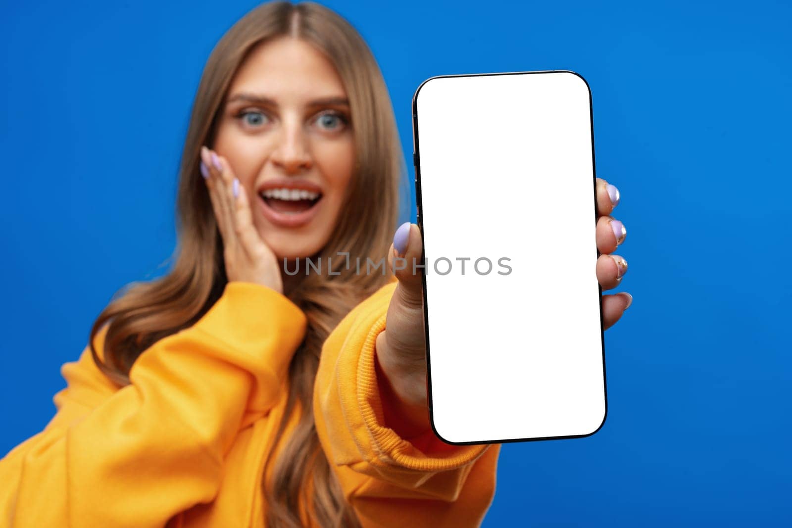 Young woman showing big blank cellphone screen on blue background in studio, copy space