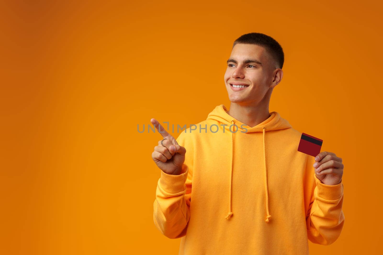 Handsome young man holding credit card on yellow color background in studio