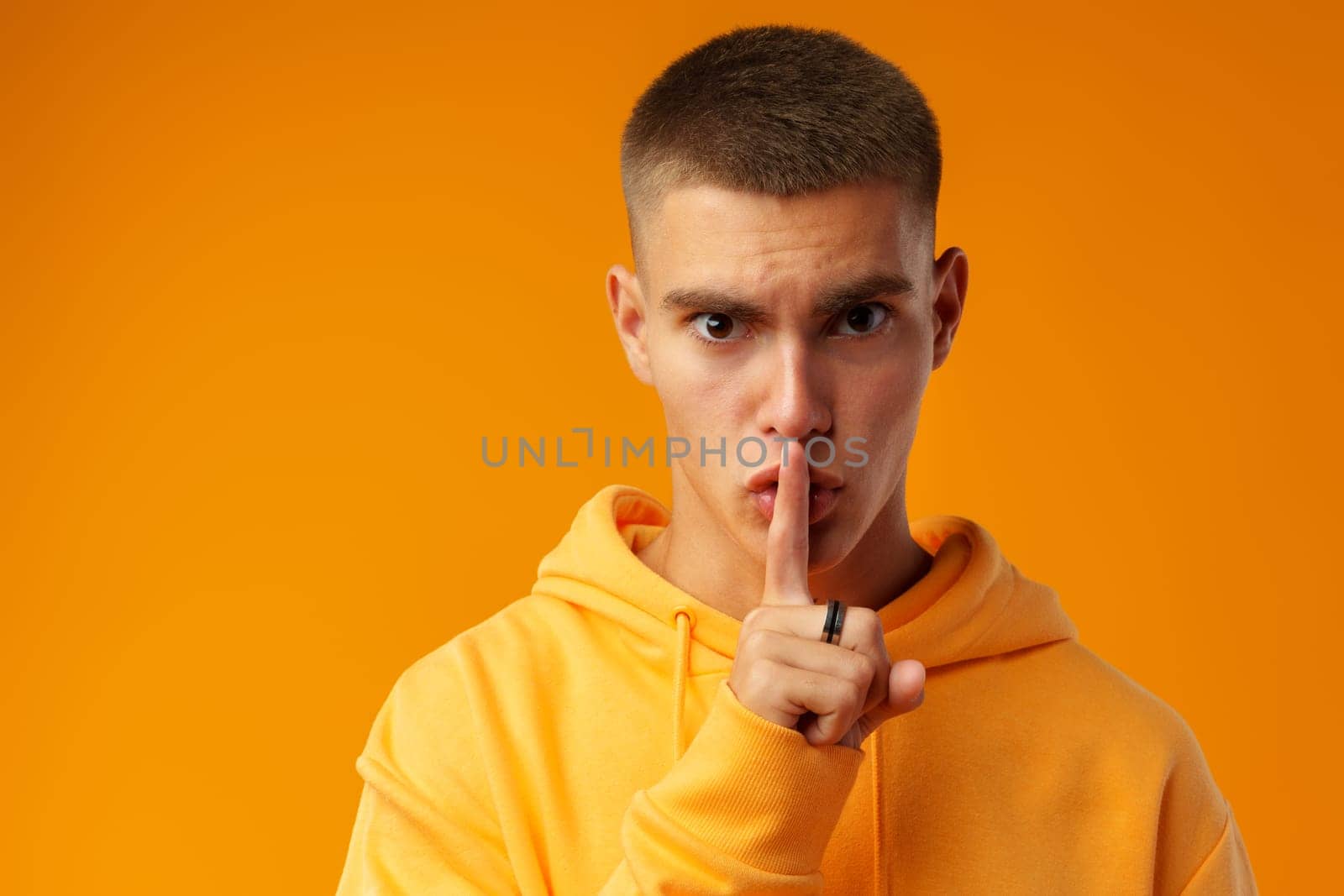 Young man making hush sign over yellow background in studio