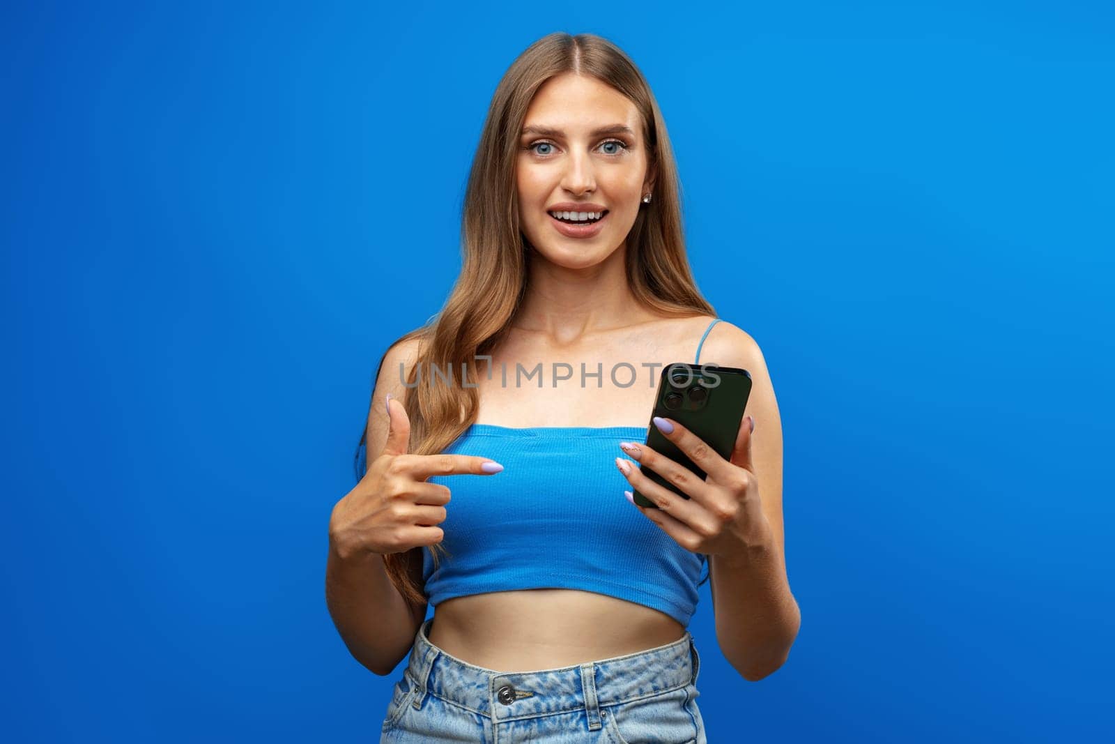 Confused young beautiful woman over blue background using mobile phone in studio