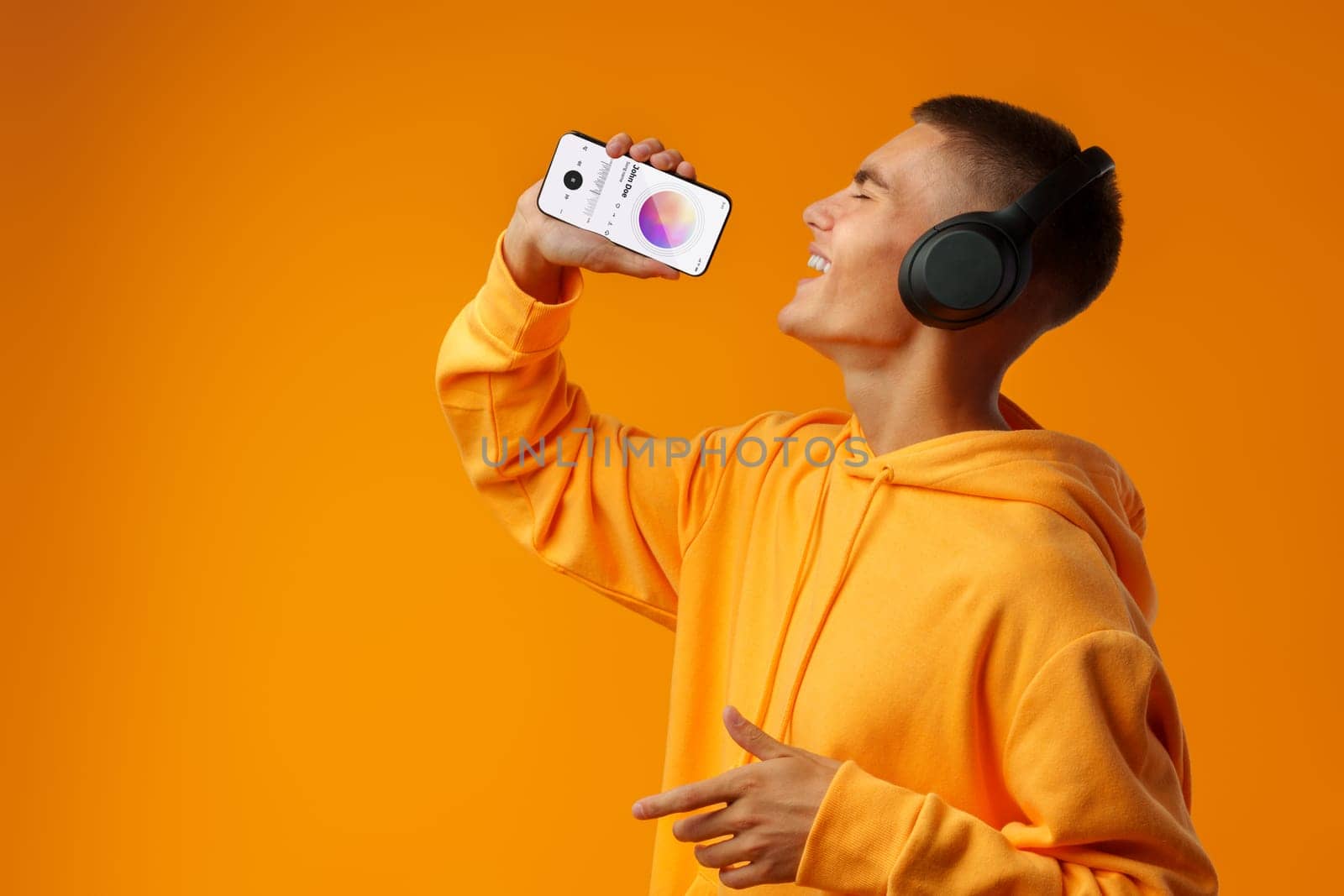 Young handsome man using smartphone as microphone against yellow background close up