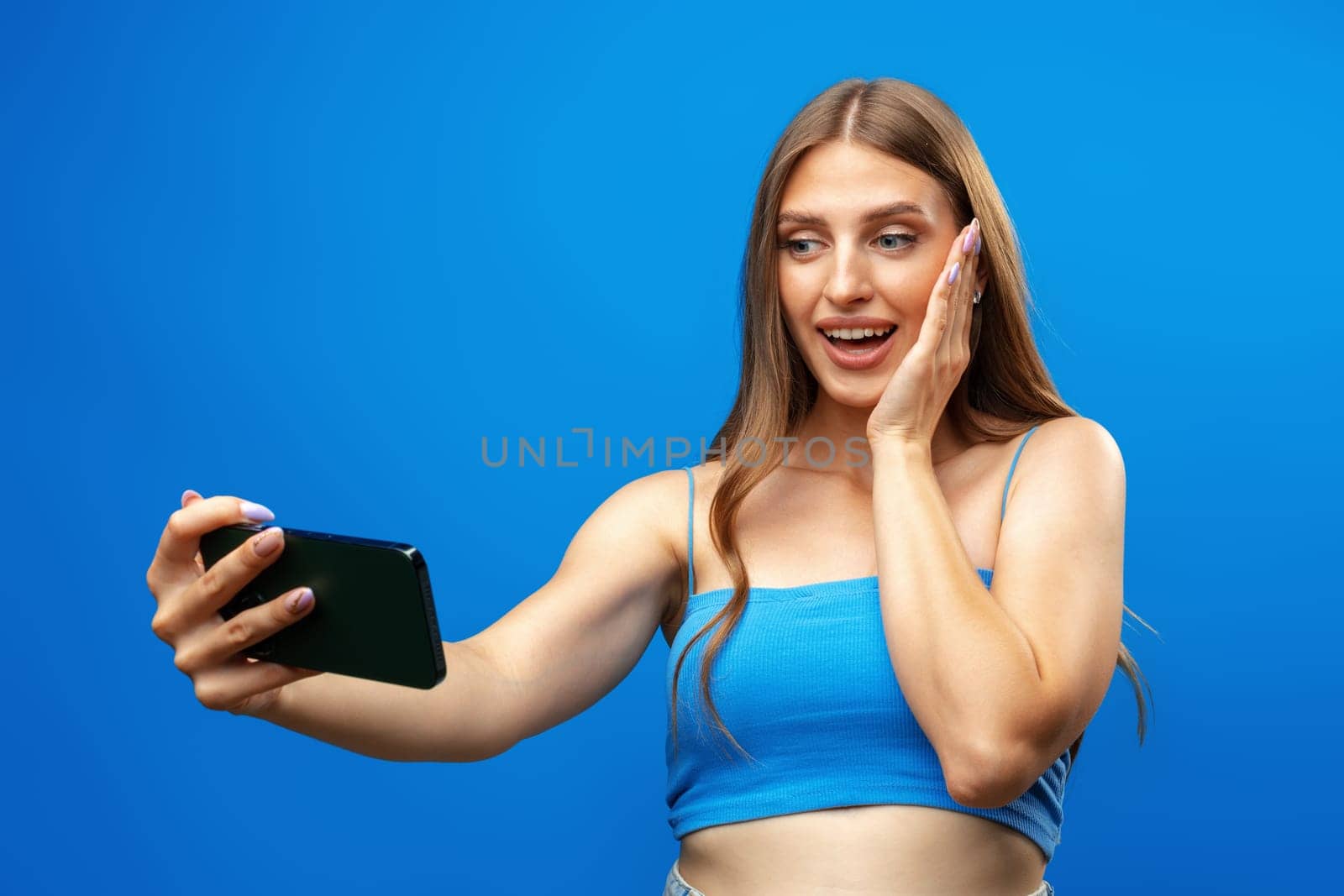 Confused young beautiful woman over blue background using mobile phone in studio