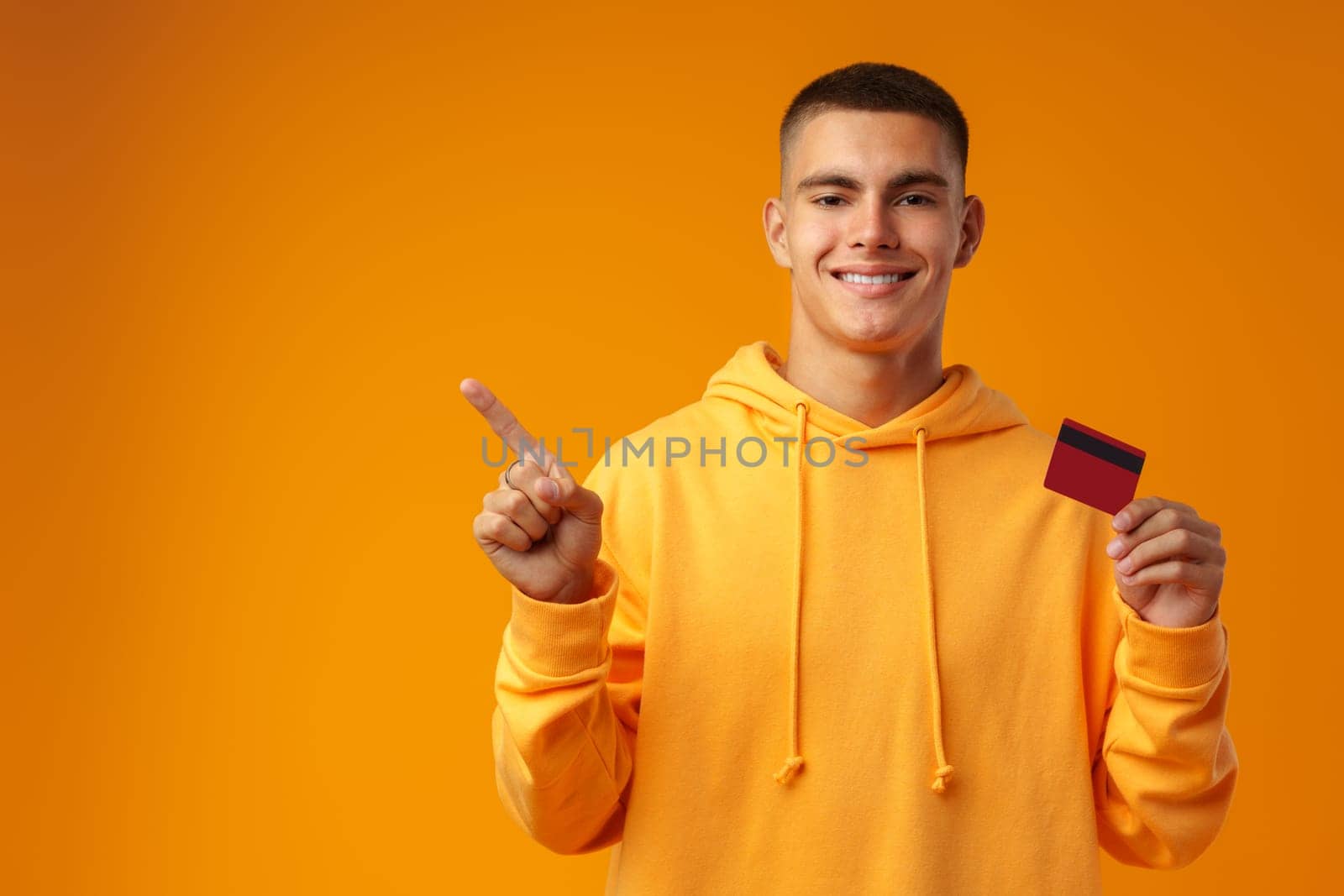 Handsome young man holding credit card on yellow color background in studio