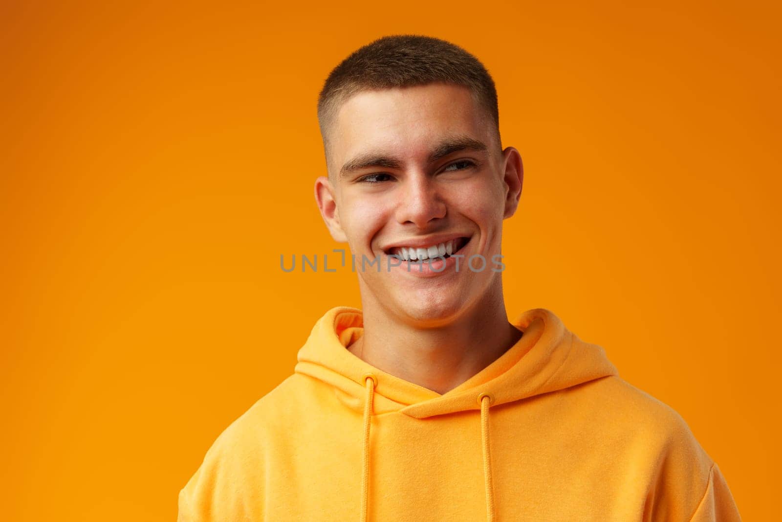 Happy smiling young man looking to camera over yellow background, close up