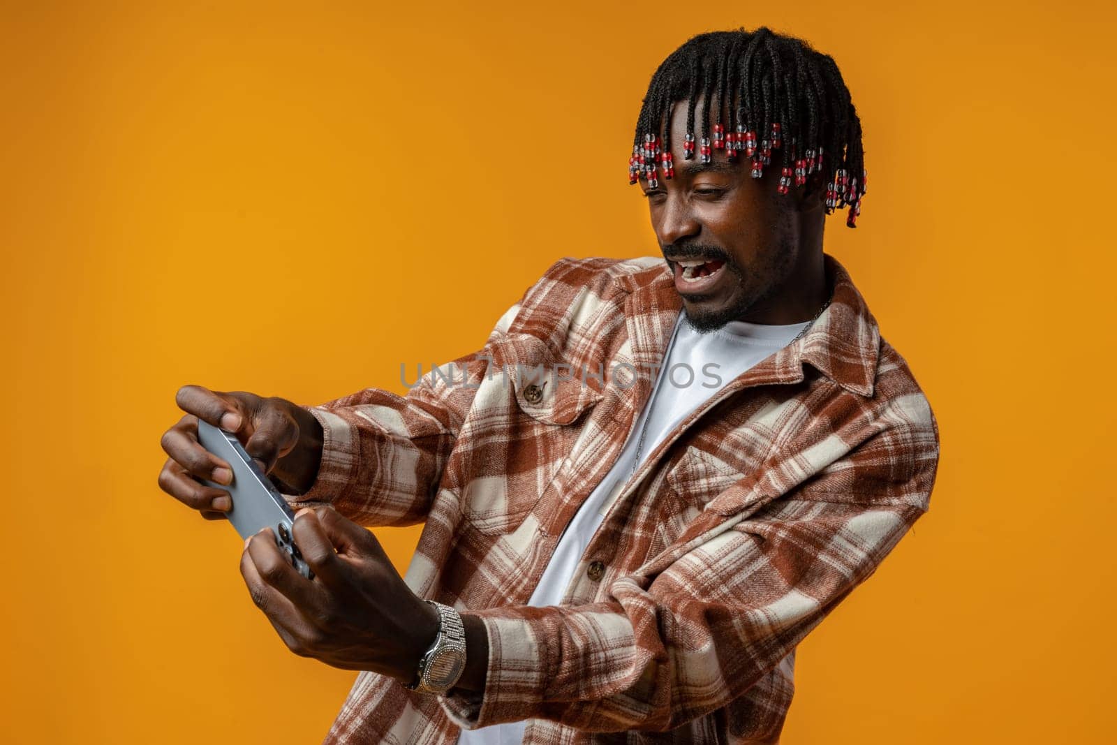 Young african man dressed in casual playing games on mobile phone over yellow background, close up