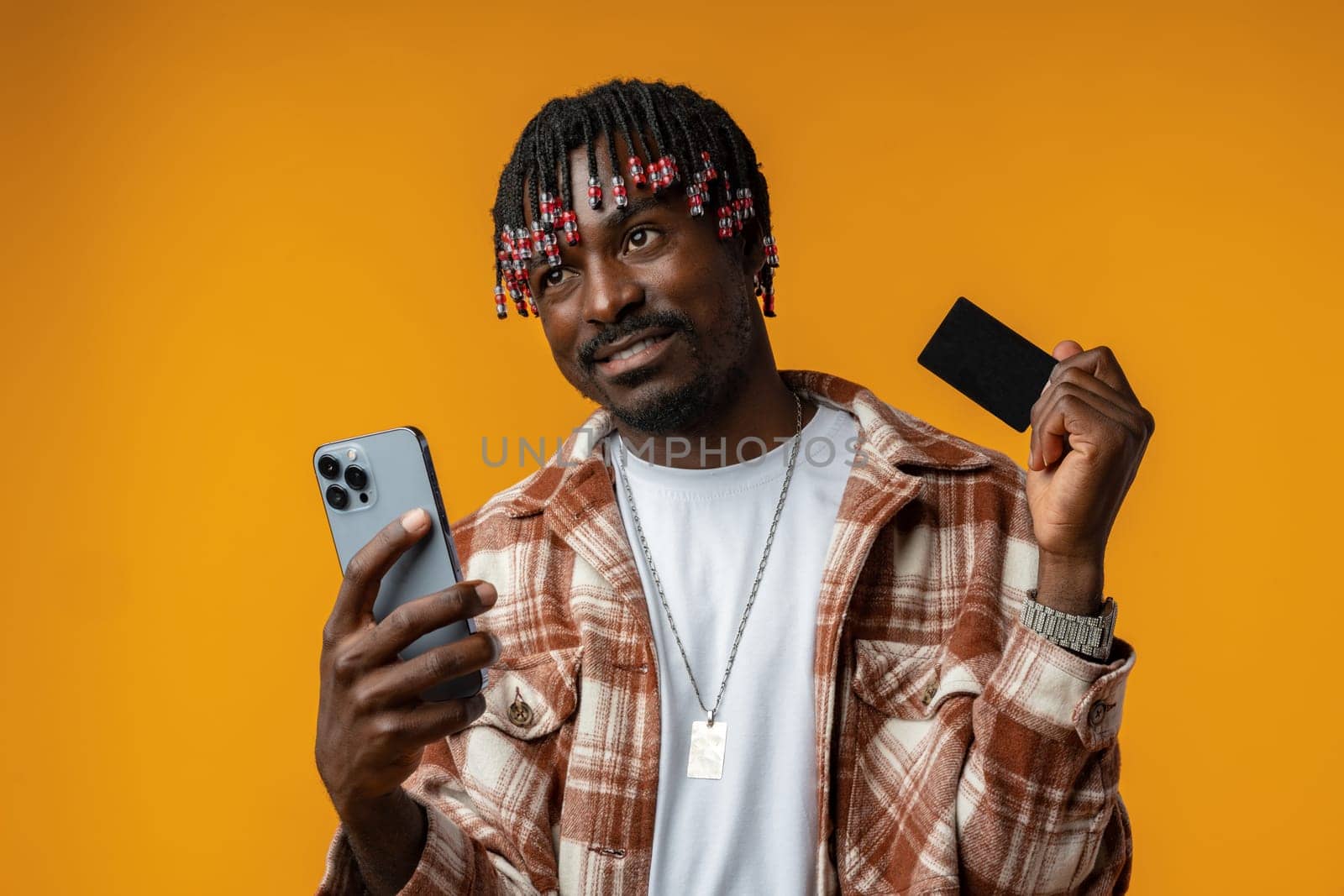 Smiling young african man on yellow background using mobile phone and holding credit card, close up