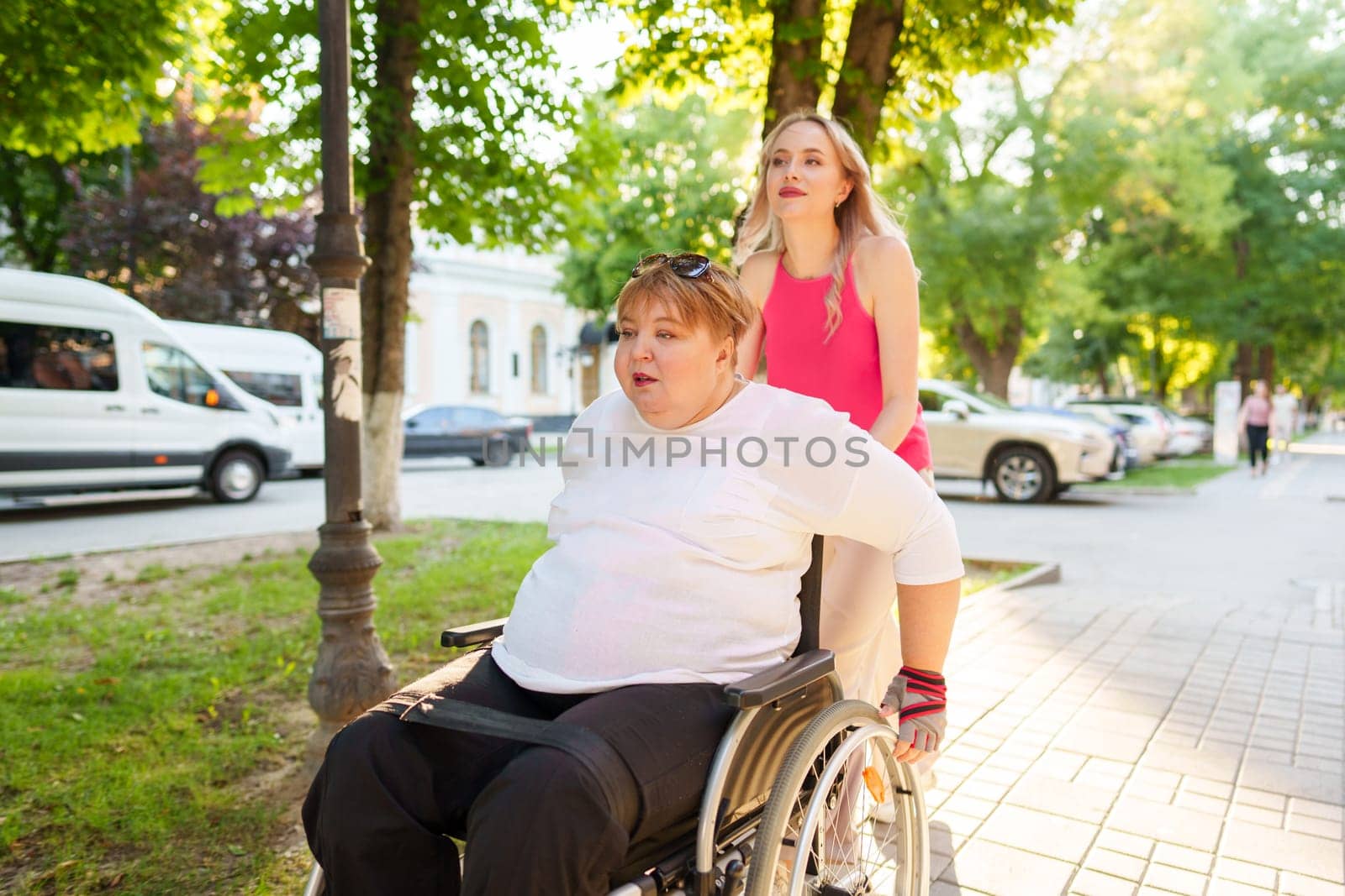 Young female caregiver pushing wheelchair with mature female person with disability across city street