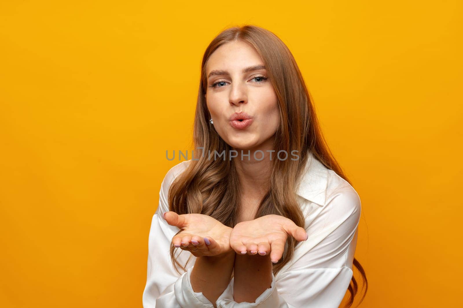 Portrait of cute lovely girl in casual outfit blowing kiss and looking at camera on yellow background, close up