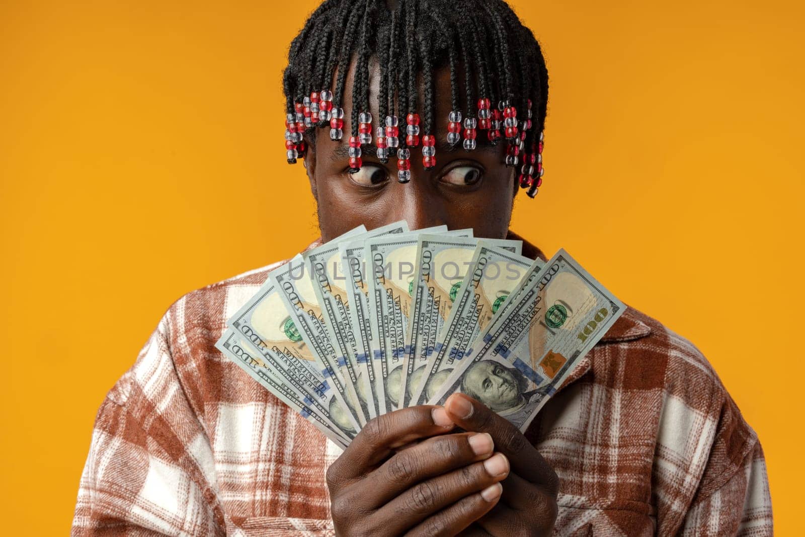 Young happy rich african man in casual shirt holding dollar bills against yellow background close up