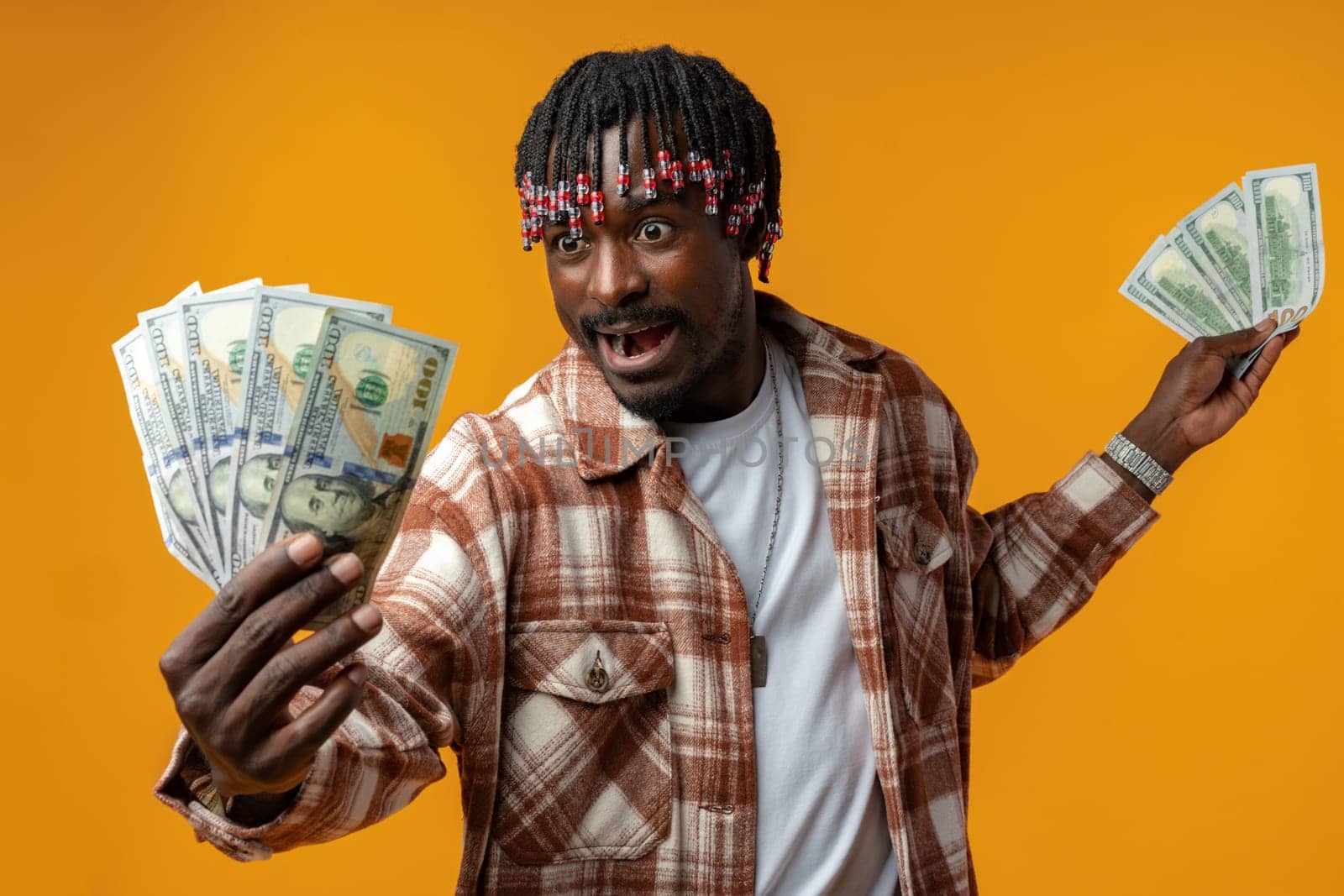 Young happy rich african man in casual shirt holding dollar bills against yellow background close up