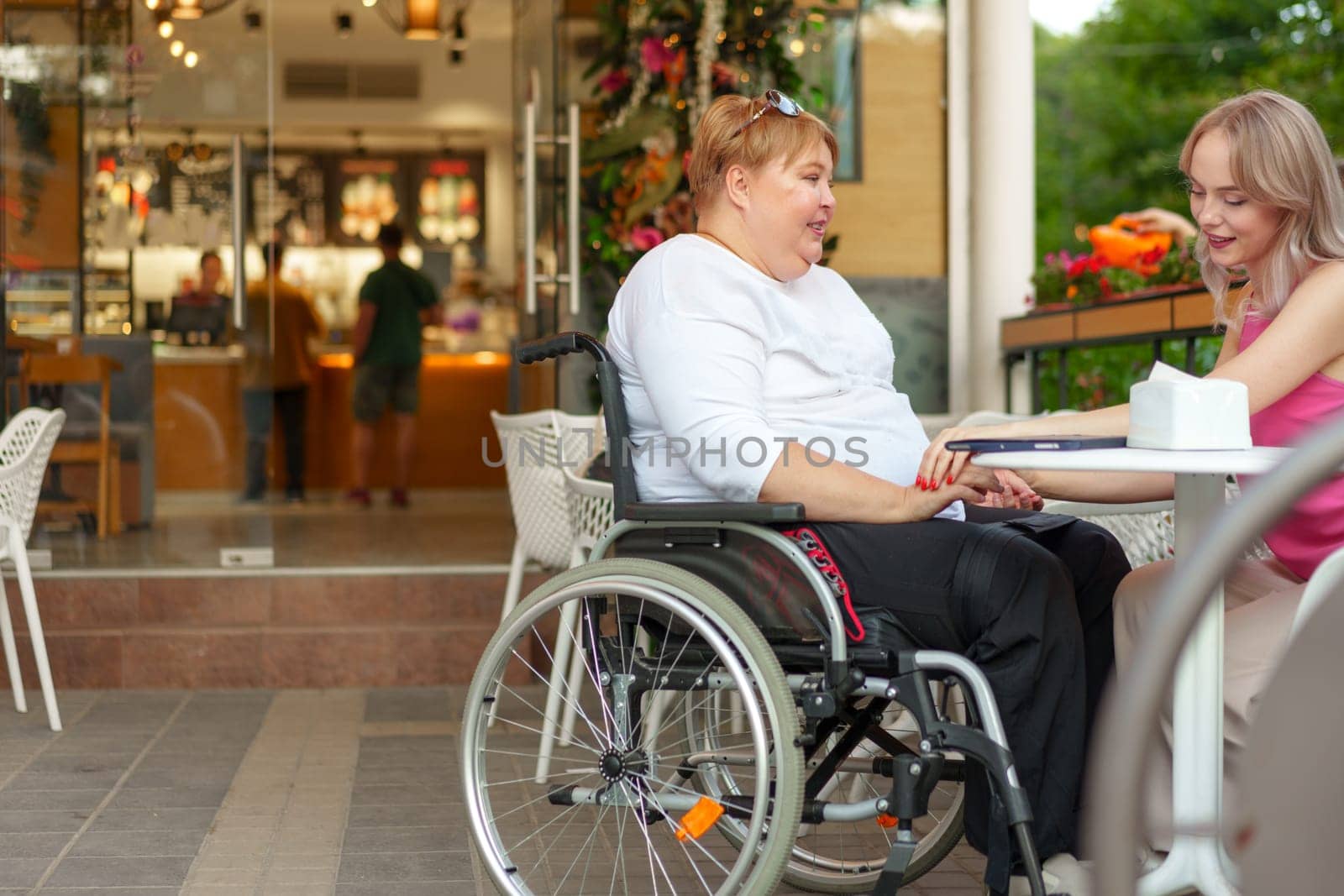 Woman with disability sitting in a wheelchair in outdoor cafe with her young daughter together