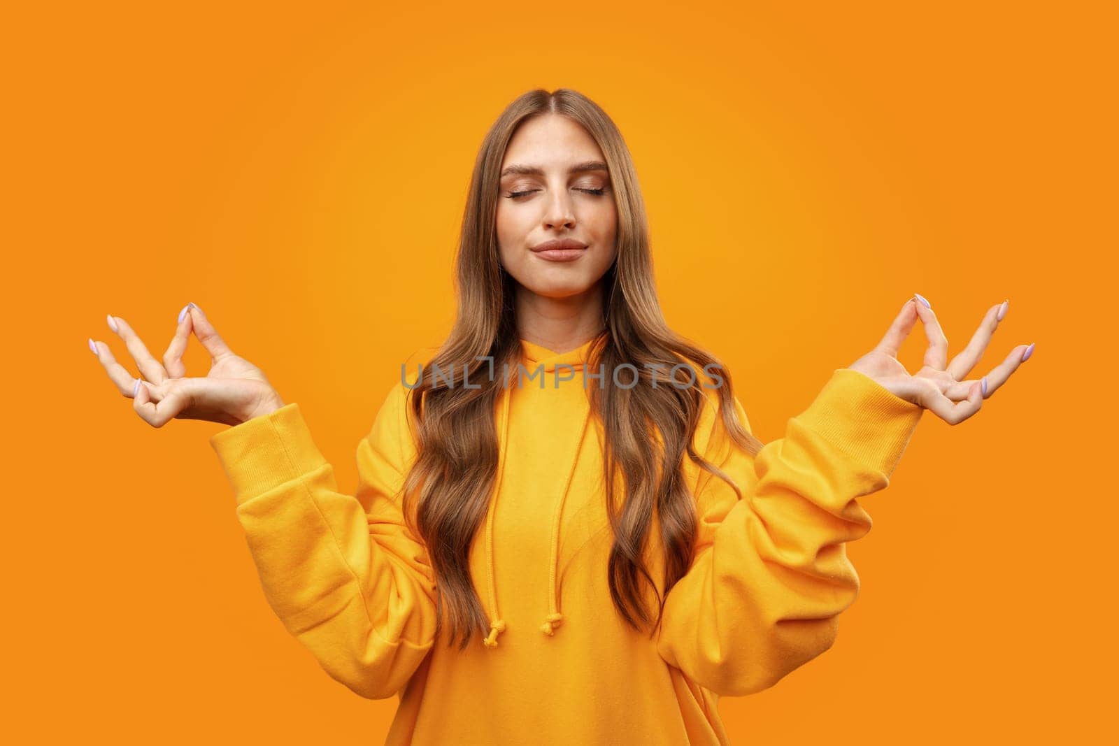 Young blonde woman making zen pose while meditating on yellow background close up