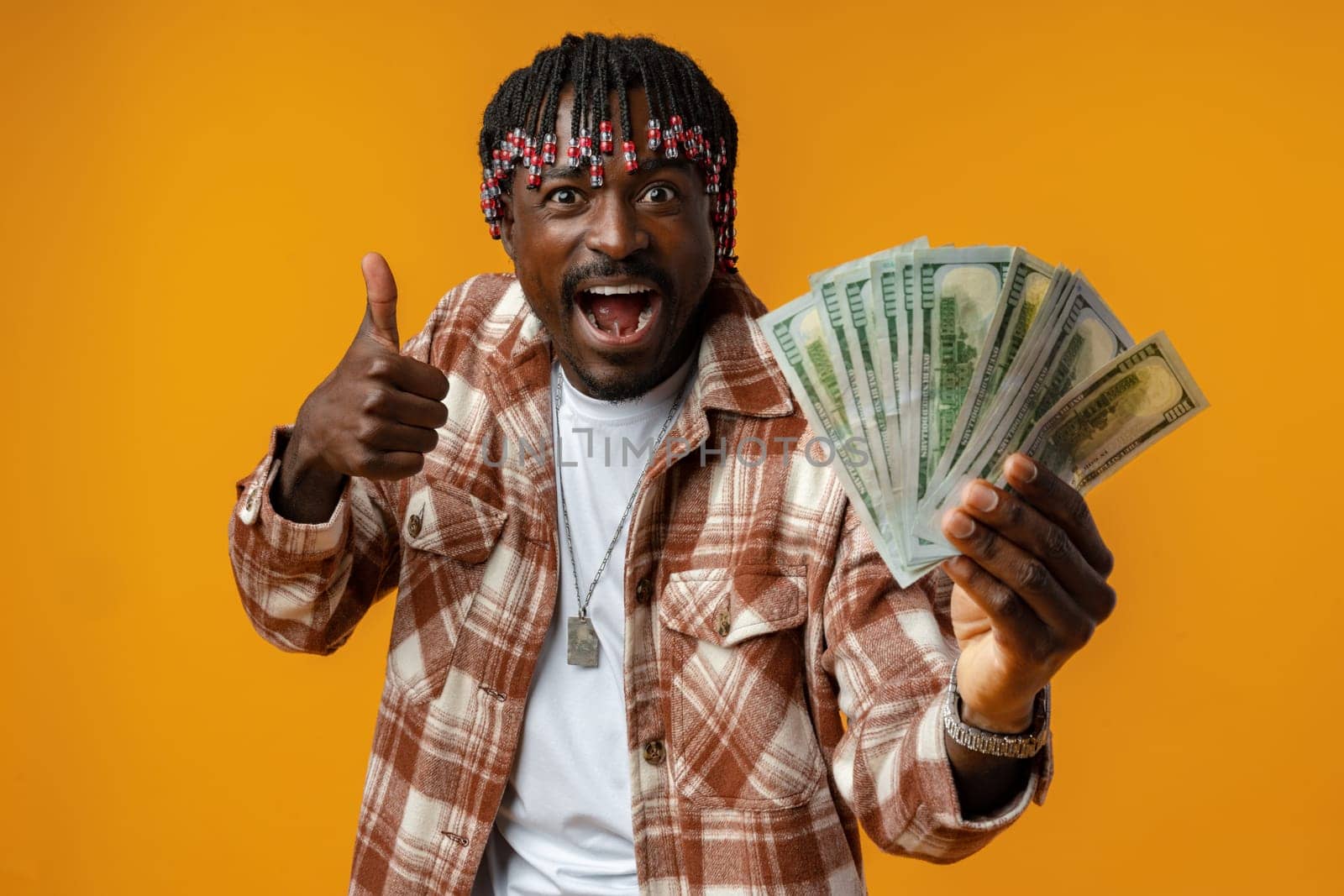 Young happy rich african man in casual shirt holding dollar bills against yellow background close up