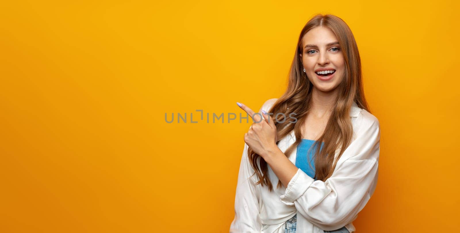 Young pretty woman pointing at copy space in photo studio