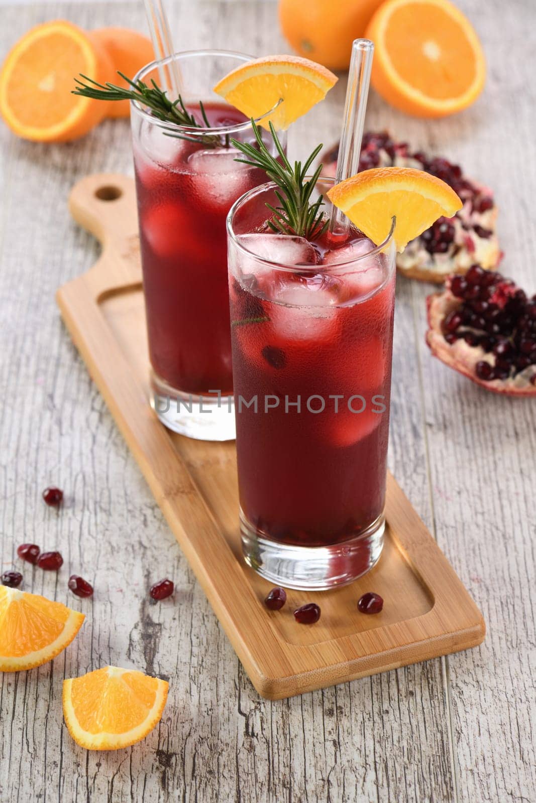 Pomegranate orange holiday punch with ice and rosemary. This is a sweet, tart and refreshing cocktail perfect for celebrating any party.