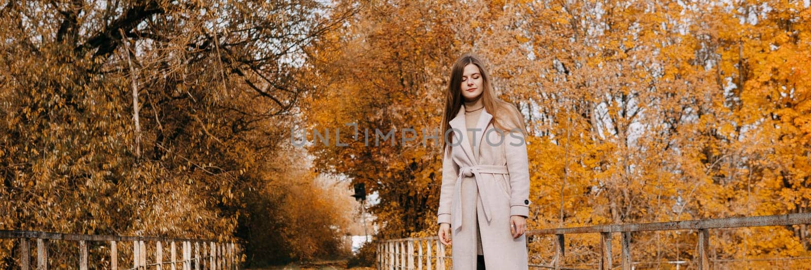 A beautiful long-haired woman walks through the autumn streets. Railway, autumn leaves, a woman in a light coat.