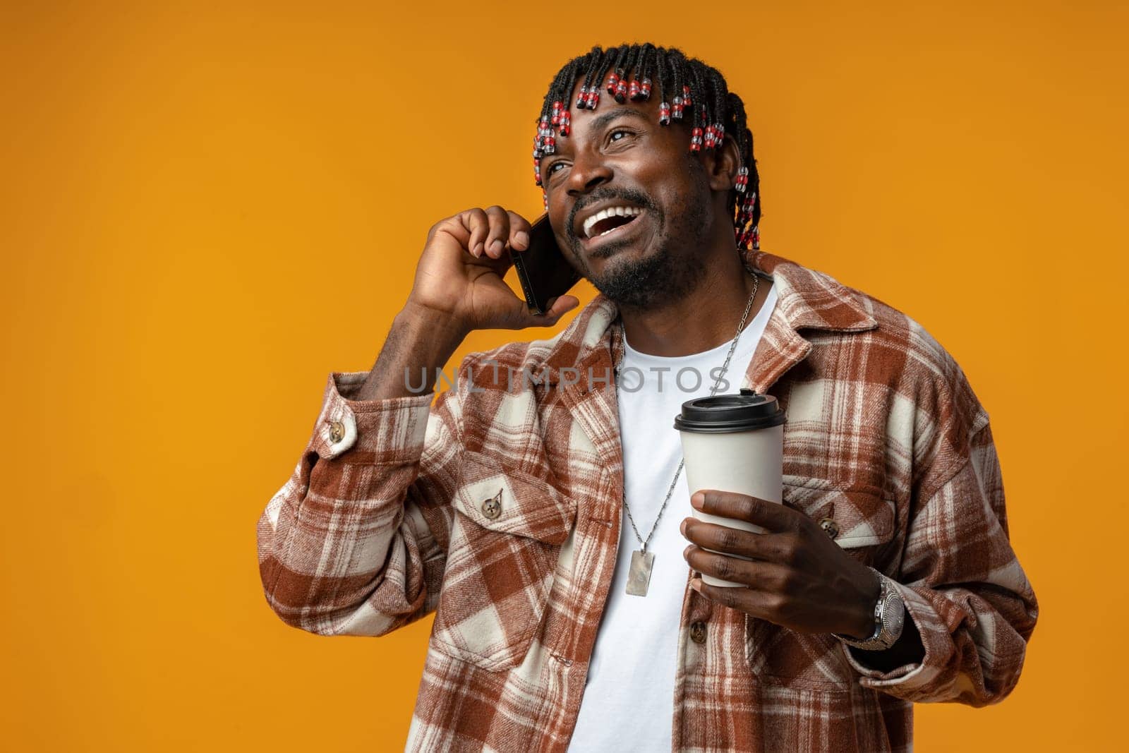 Cheerful african man talking on phone over yellow studio background close up