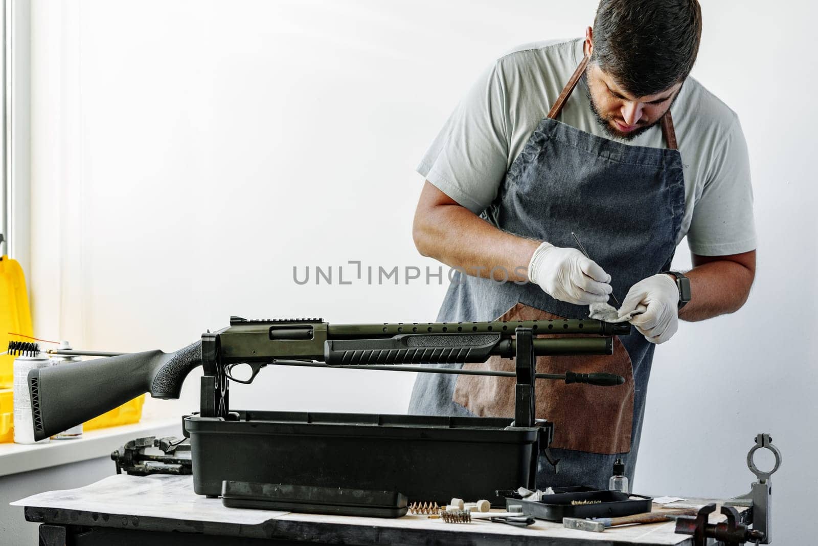 Close up of a man in apron wiping his firearm with a cloth in a workshop