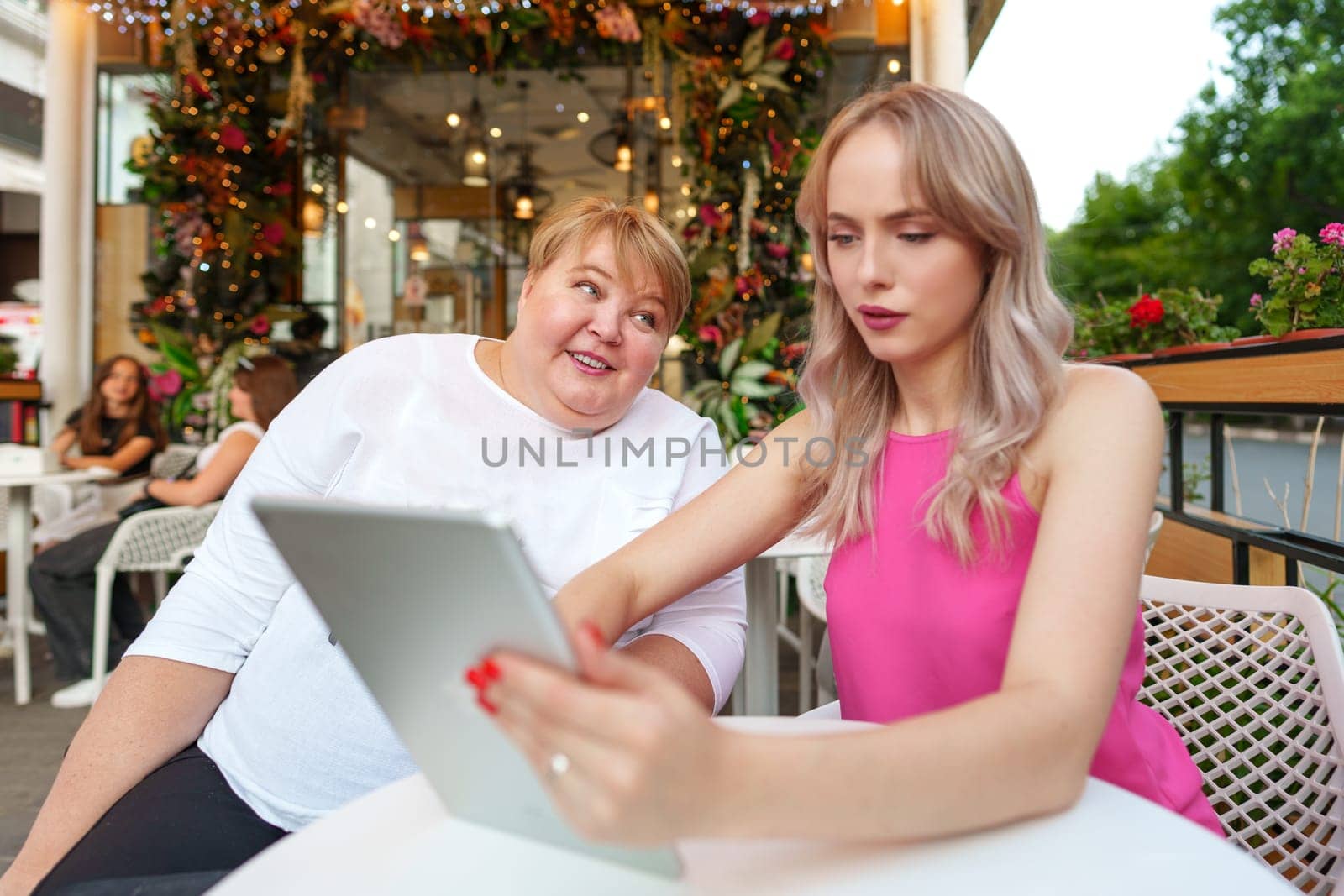 Mother with disability in wheelchair and her daughter using digital tablet while sitting at the table in cafe close up