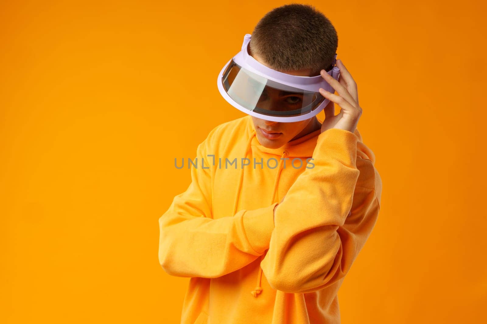 Young urban style man in sweatshirt and visor on yellow studio background, close up