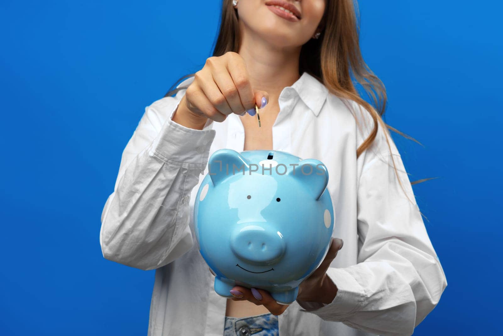 Young caucasian woman holding a piggy bank.against blue background in studio