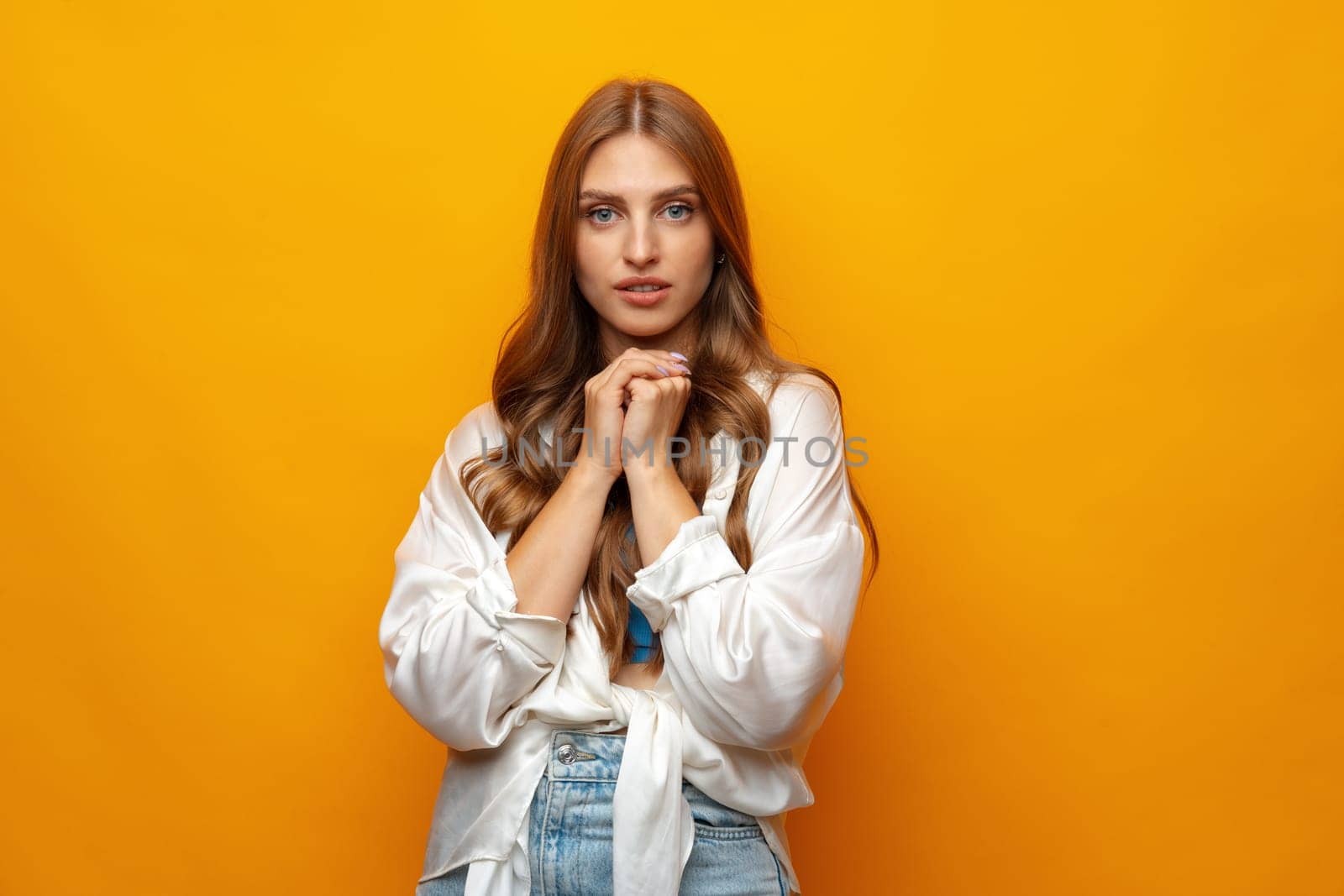 Charming blonde woman stands on yellow background looks directly at camera, close up