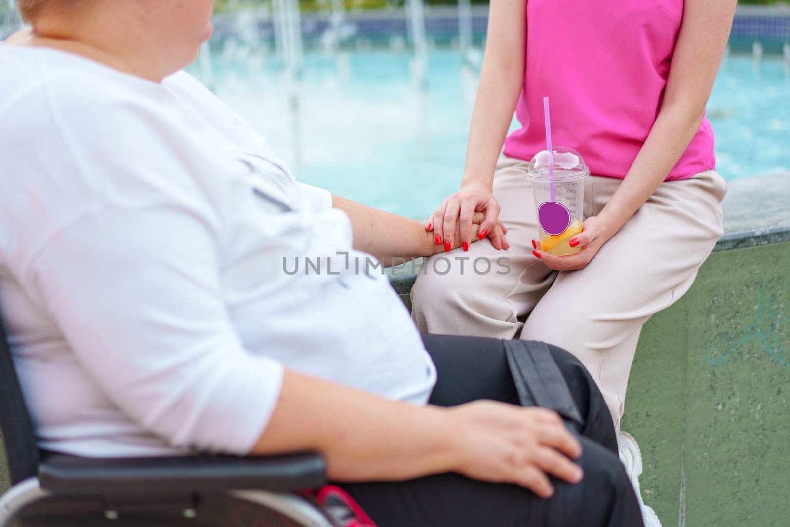 Senior woman in wheelchair holding hands with caretaker in the street close up