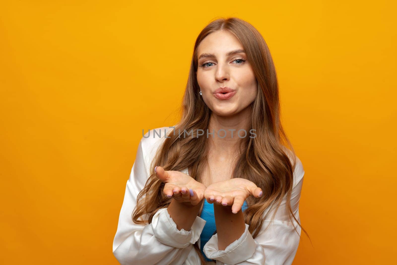 Portrait of cute lovely girl in casual outfit blowing kiss and looking at camera on yellow background, close up