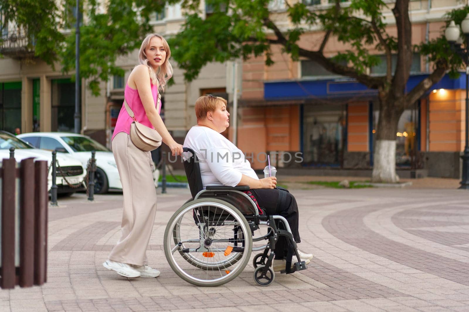 Young woman helping mature woman in wheelchair in the city street