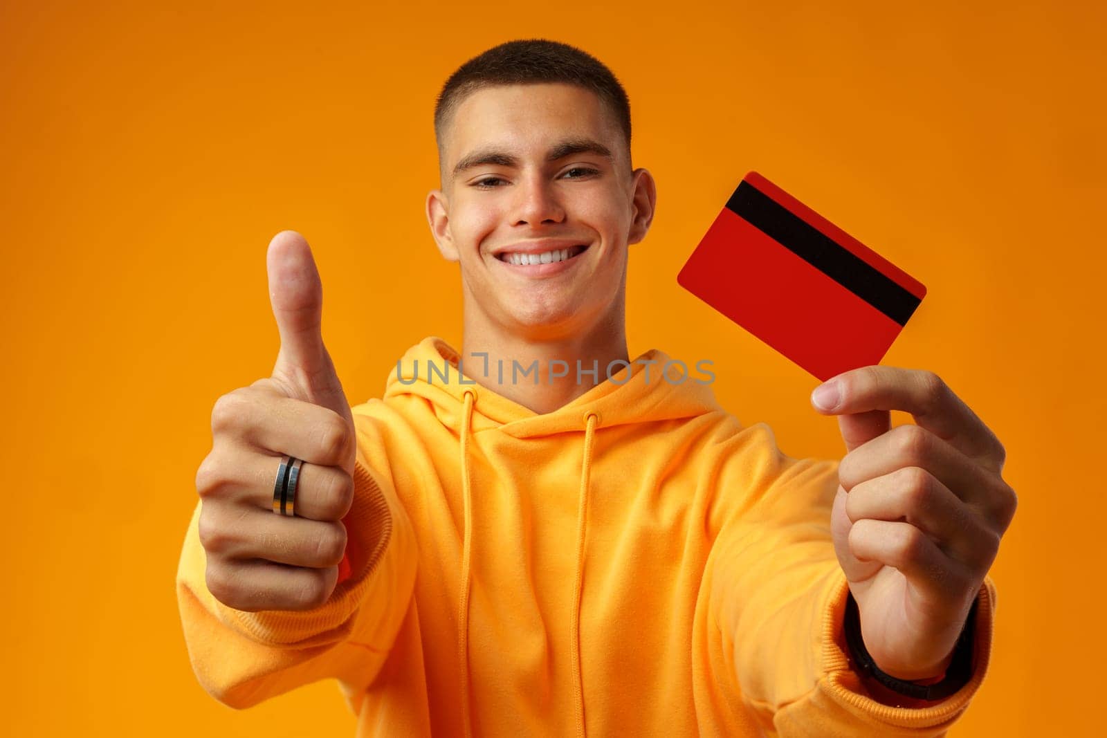 Handsome young man holding credit card on yellow color background in studio