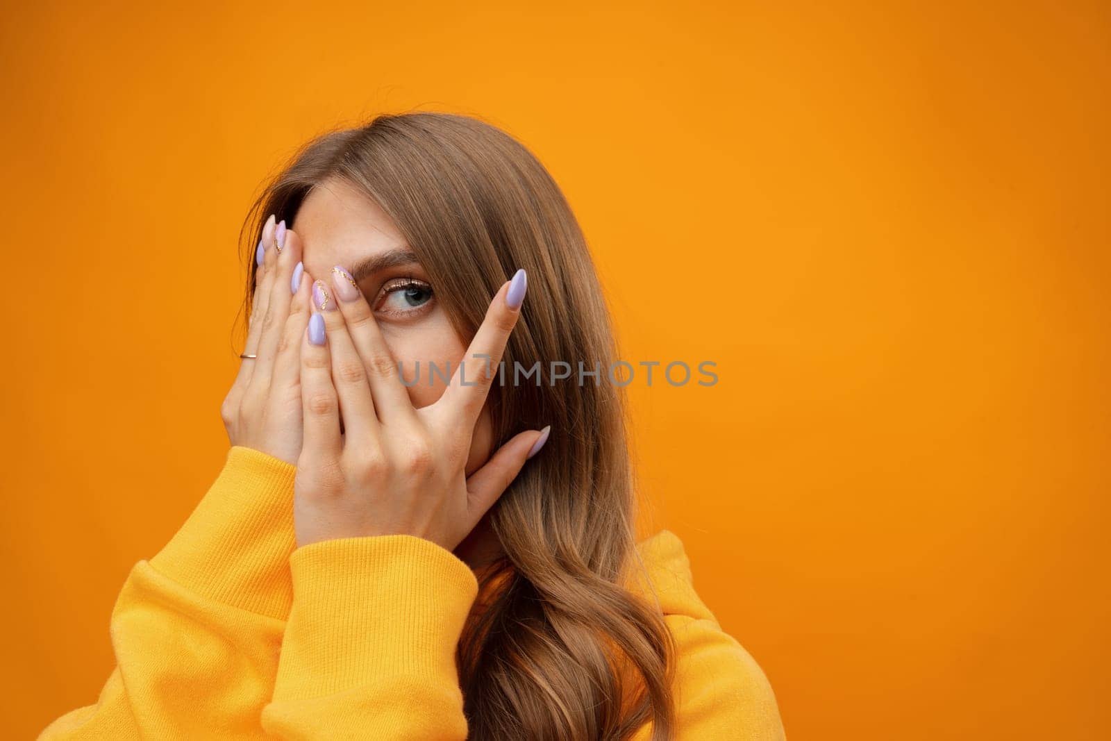 Young woman in bad mood close face by hands studio shot on yellow background, close up