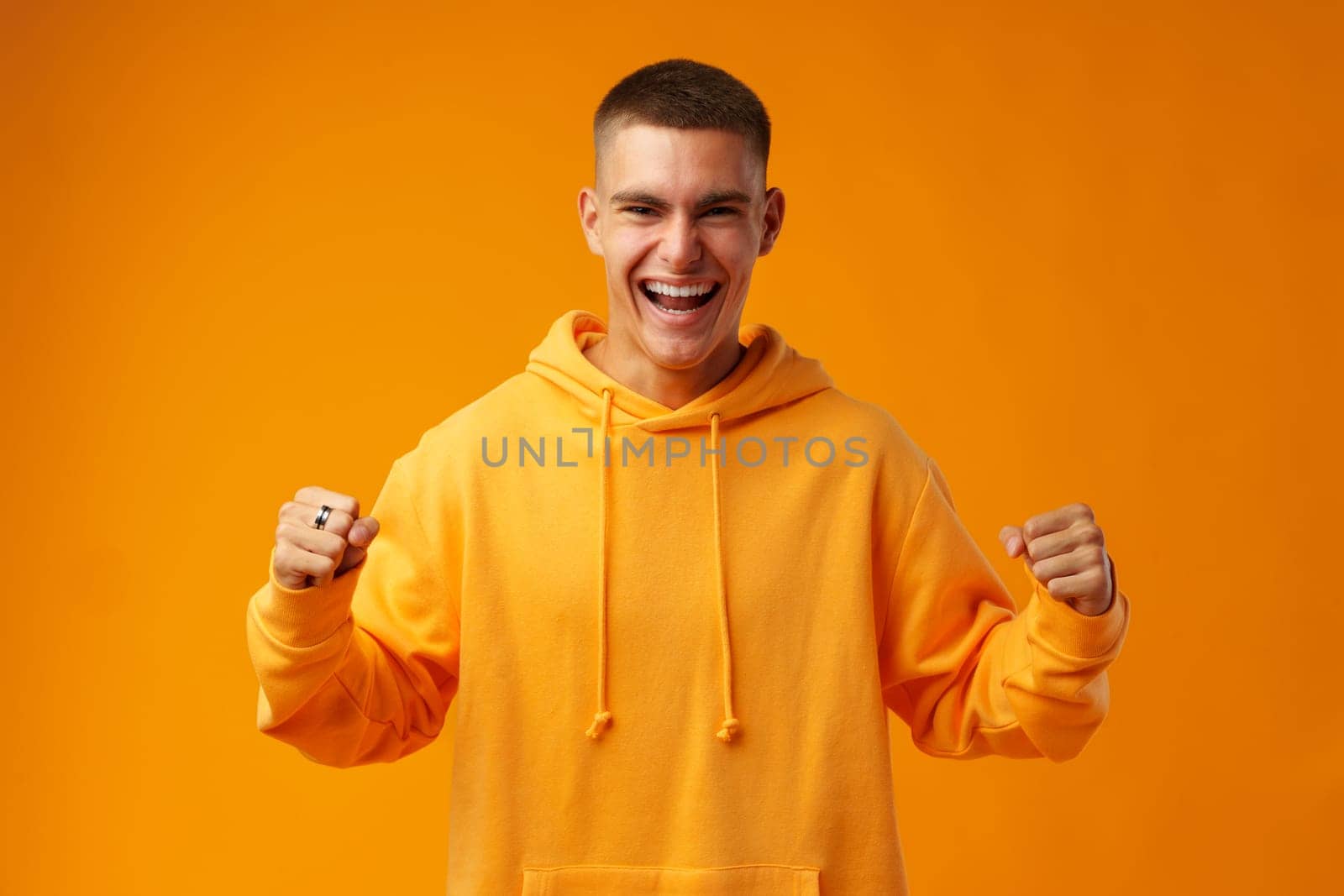 Portrait of a happy young man celebrating success against yellow background in studio