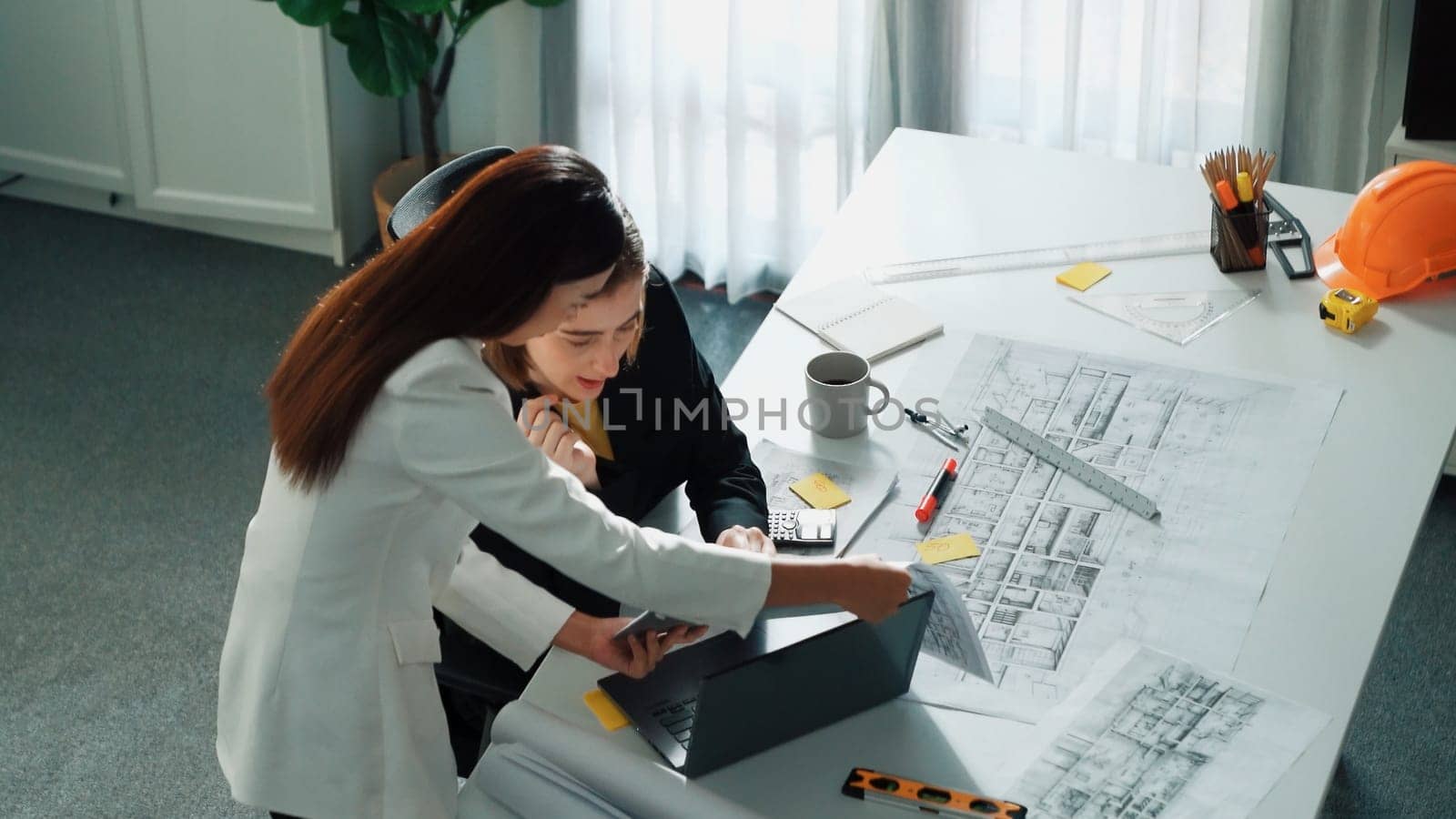 Top view of smart business woman talking and give house design. Aerial view of architect engineer looking at blueprint and building structure at table with safety helmet and house model. Alimentation.