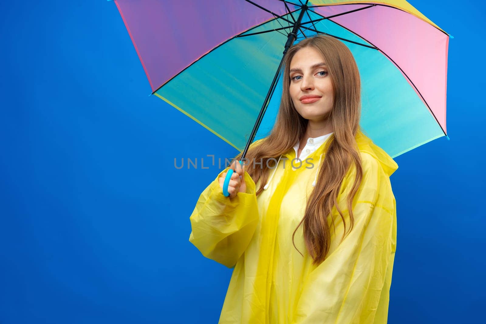 Young blonde woman wearing yellow raincoat smiling at camera over blue background in studio, close up