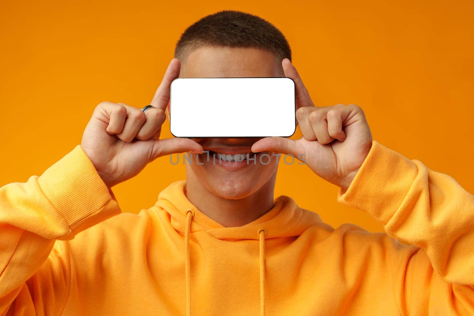 Smiling young man showing mobile phone blank white screen on yellow background copy space