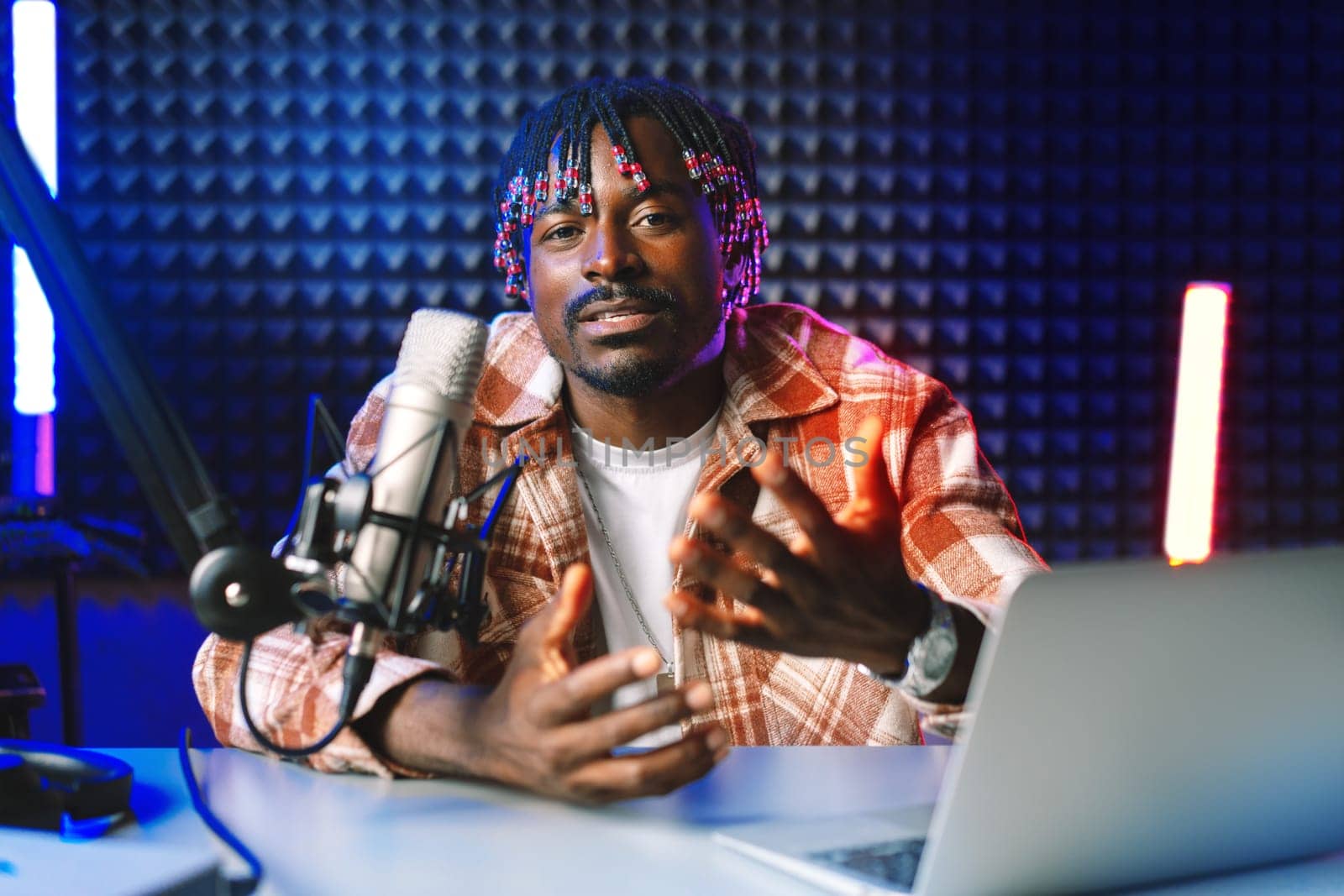 African radio host sitting at desk recording in studio with microphone and laptop close up