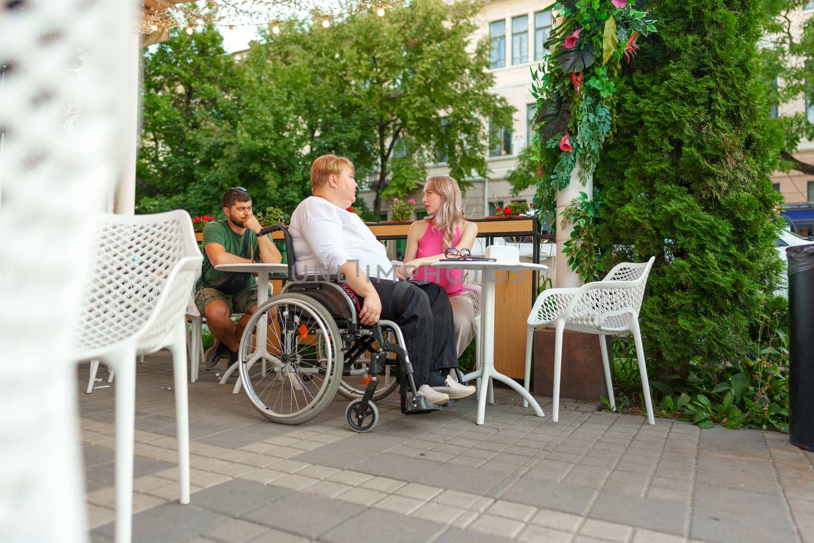 Woman with disability sitting in a wheelchair in outdoor cafe with her young daughter together