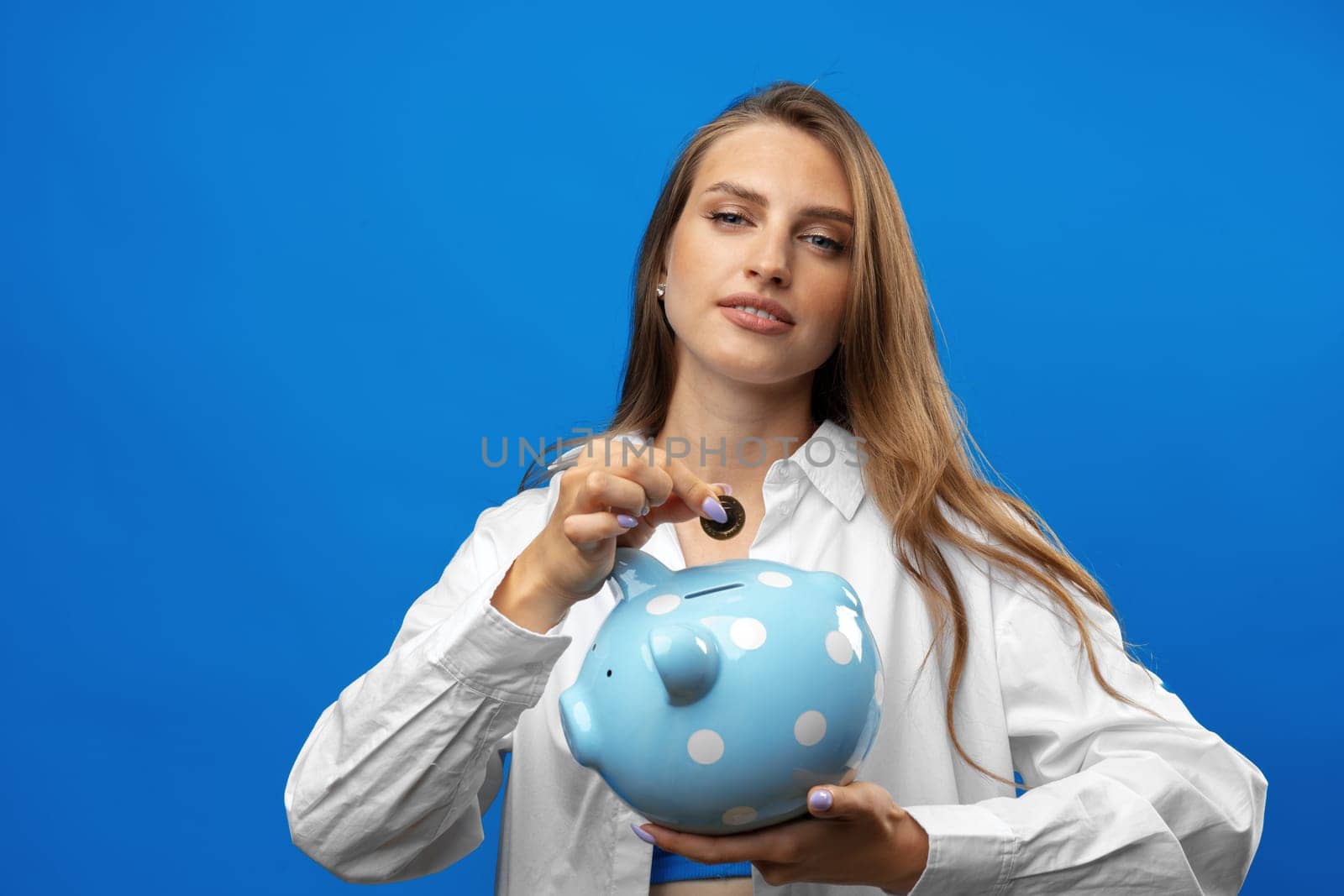 Young caucasian woman holding a piggy bank.against blue background in studio