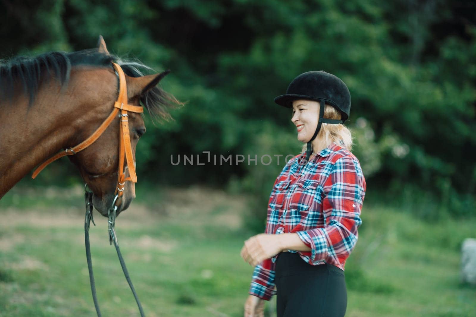 Happy blonde with horse in forest. Woman and a horse walking through the field during the day. Dressed in a plaid shirt and black leggings