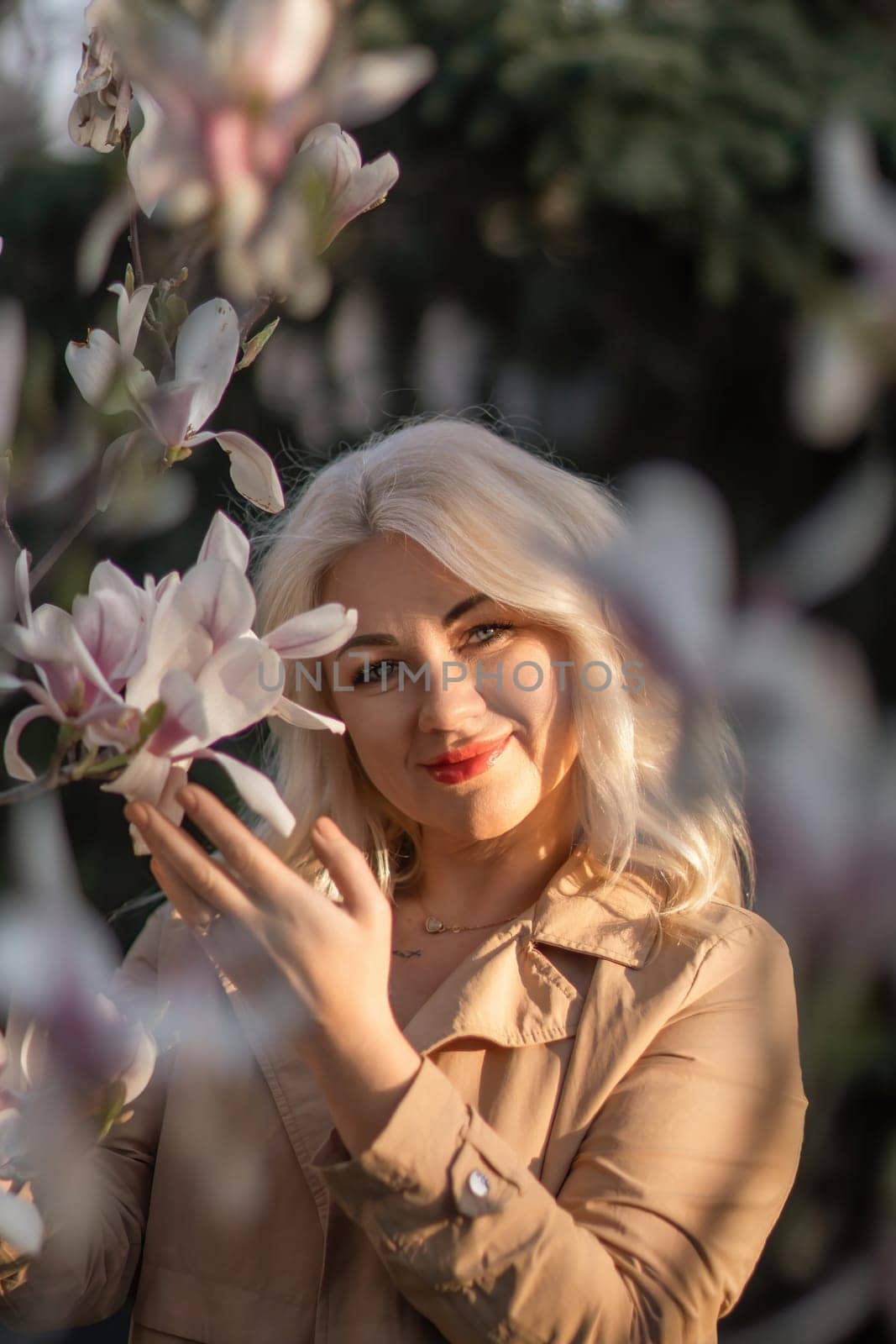 A woman is holding a magnolia flower in her hand and standing in front of a tree. Concept of serenity and beauty, as the woman is surrounded by nature and the flower adds a touch of color